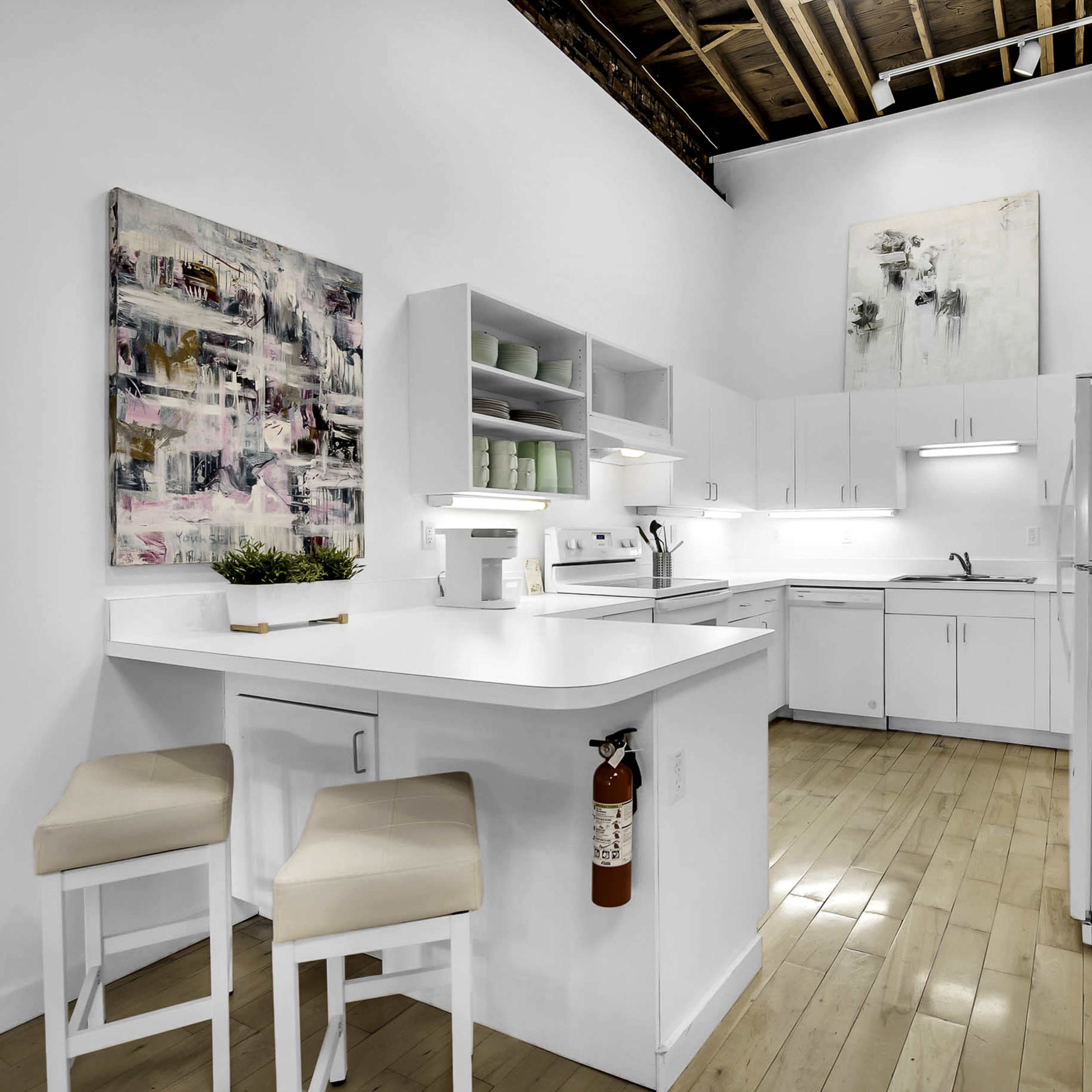 A modern kitchen featuring white cabinetry, a central island with seating, and a mix of artwork on the walls.