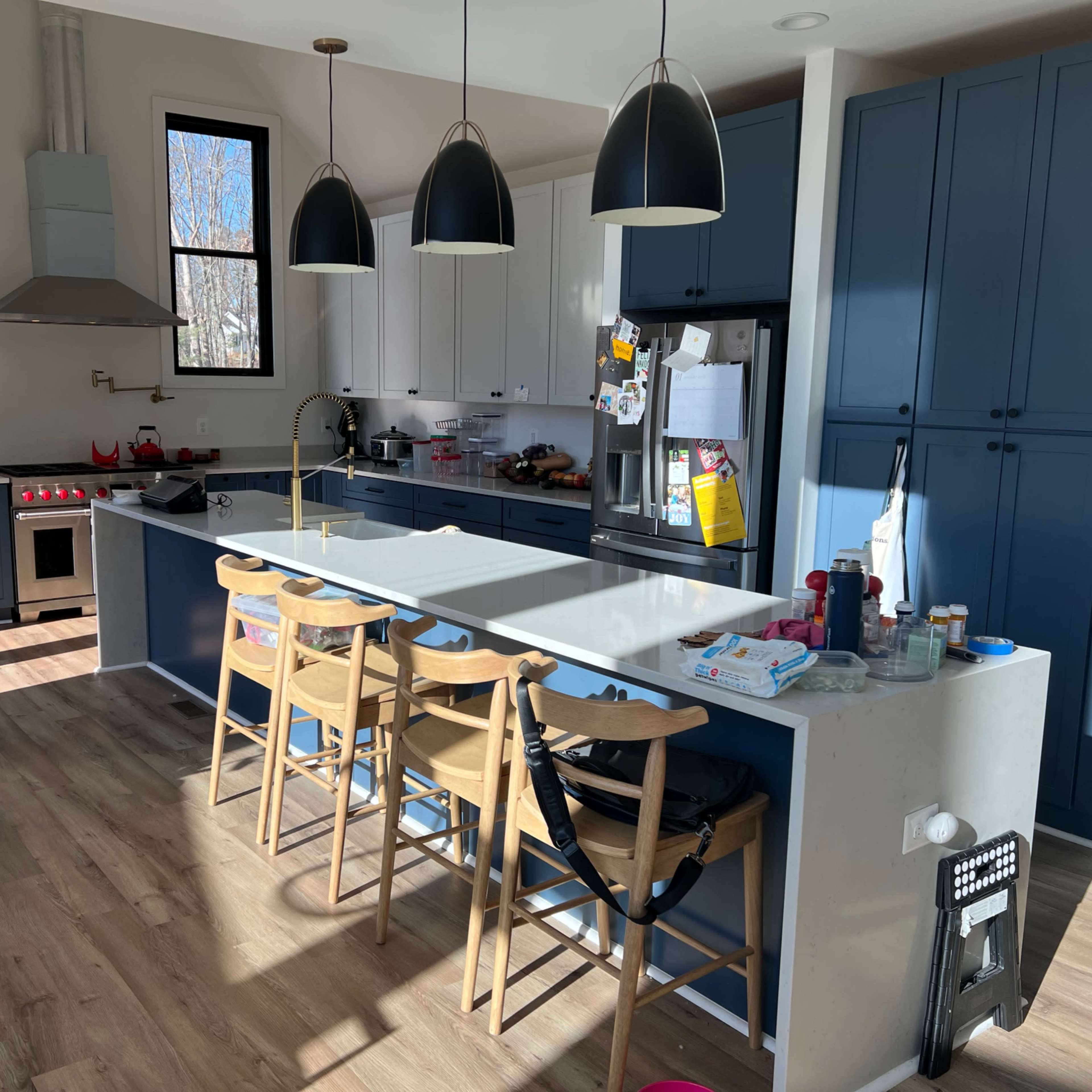 The kitchen features a long island with barstools, dual-tone cabinets, and pendant lights hanging above.