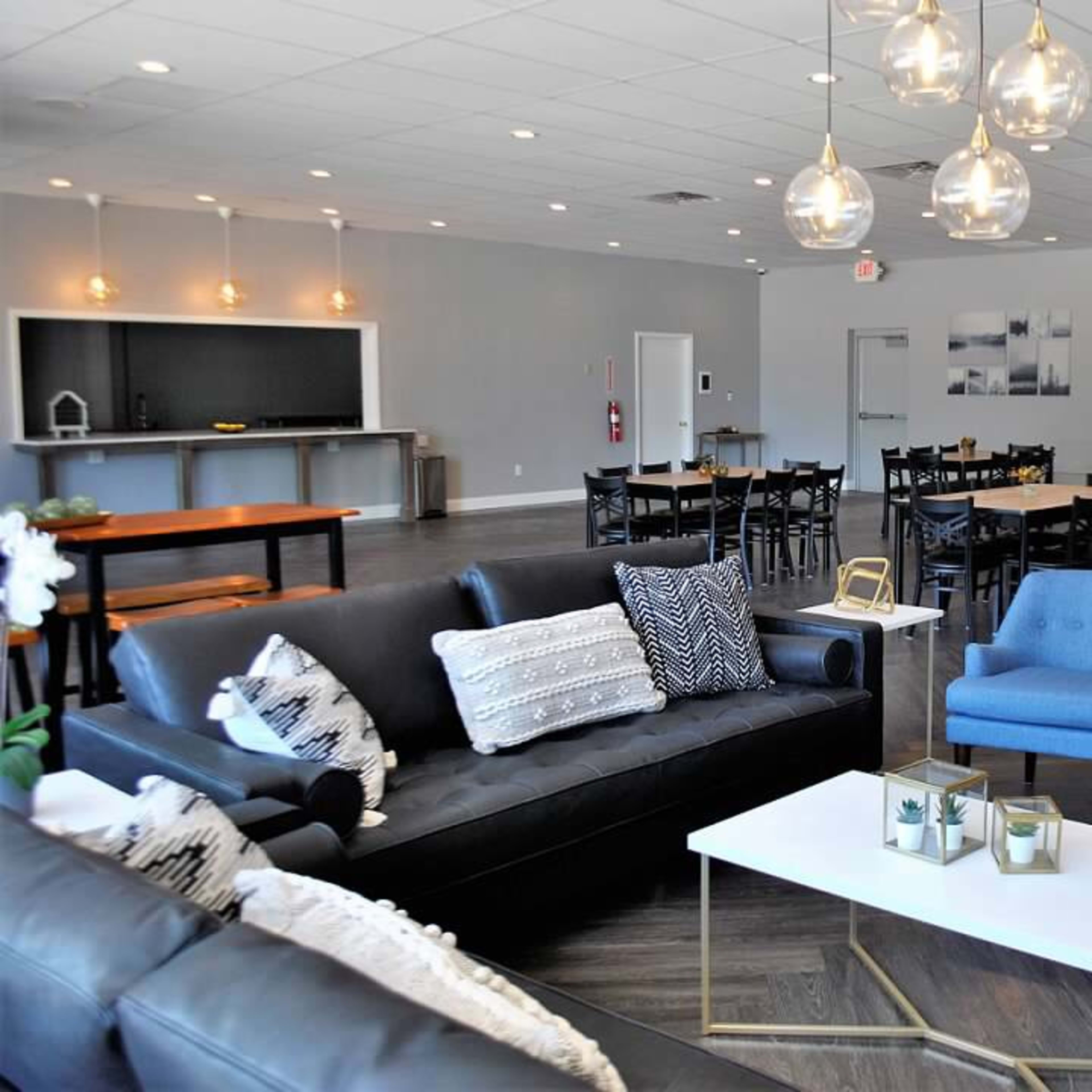 A spacious, modern event room with a seating area featuring a black sofa and blue chairs, alongside tables arranged for dining.
