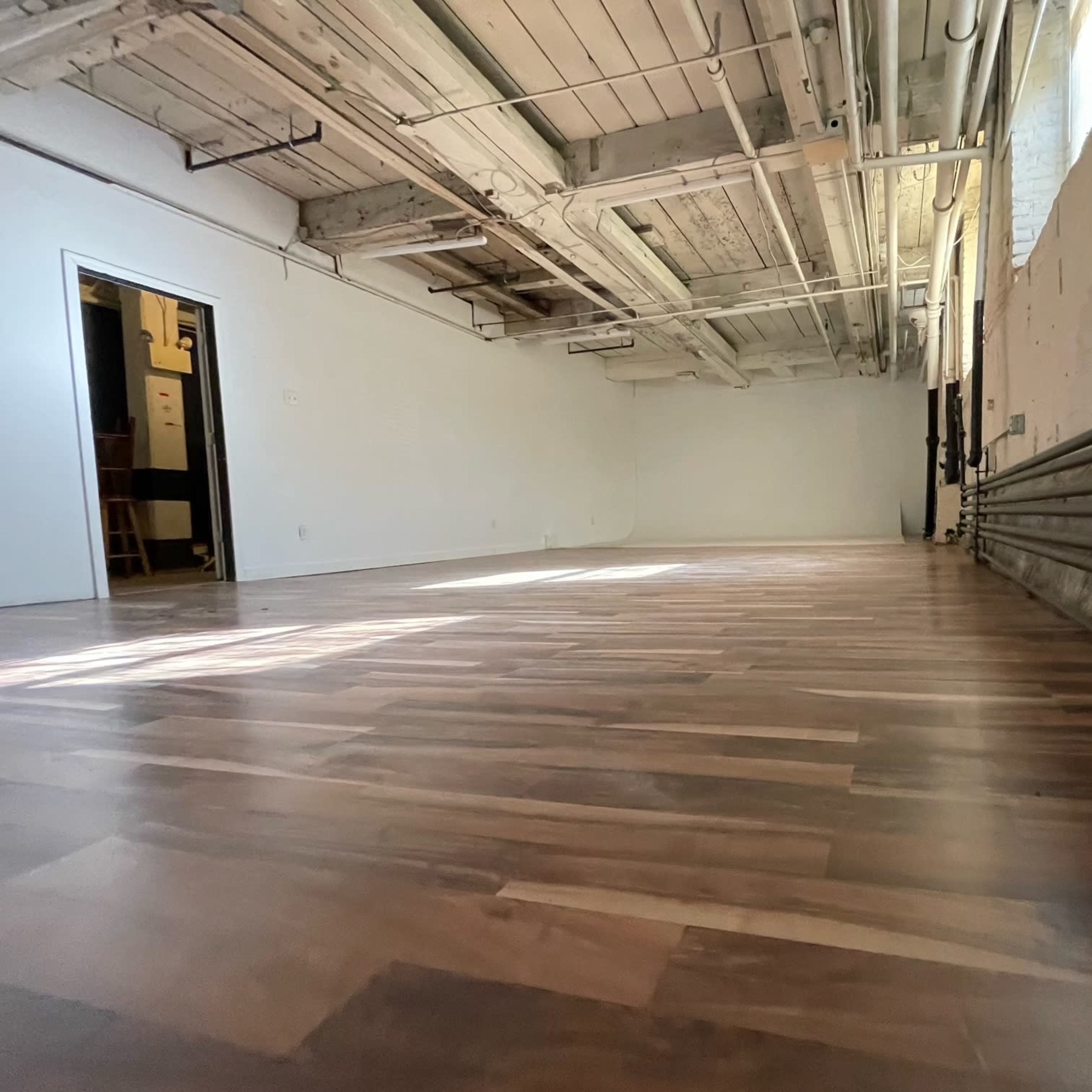 An empty room with polished wooden flooring and exposed ceiling beams.