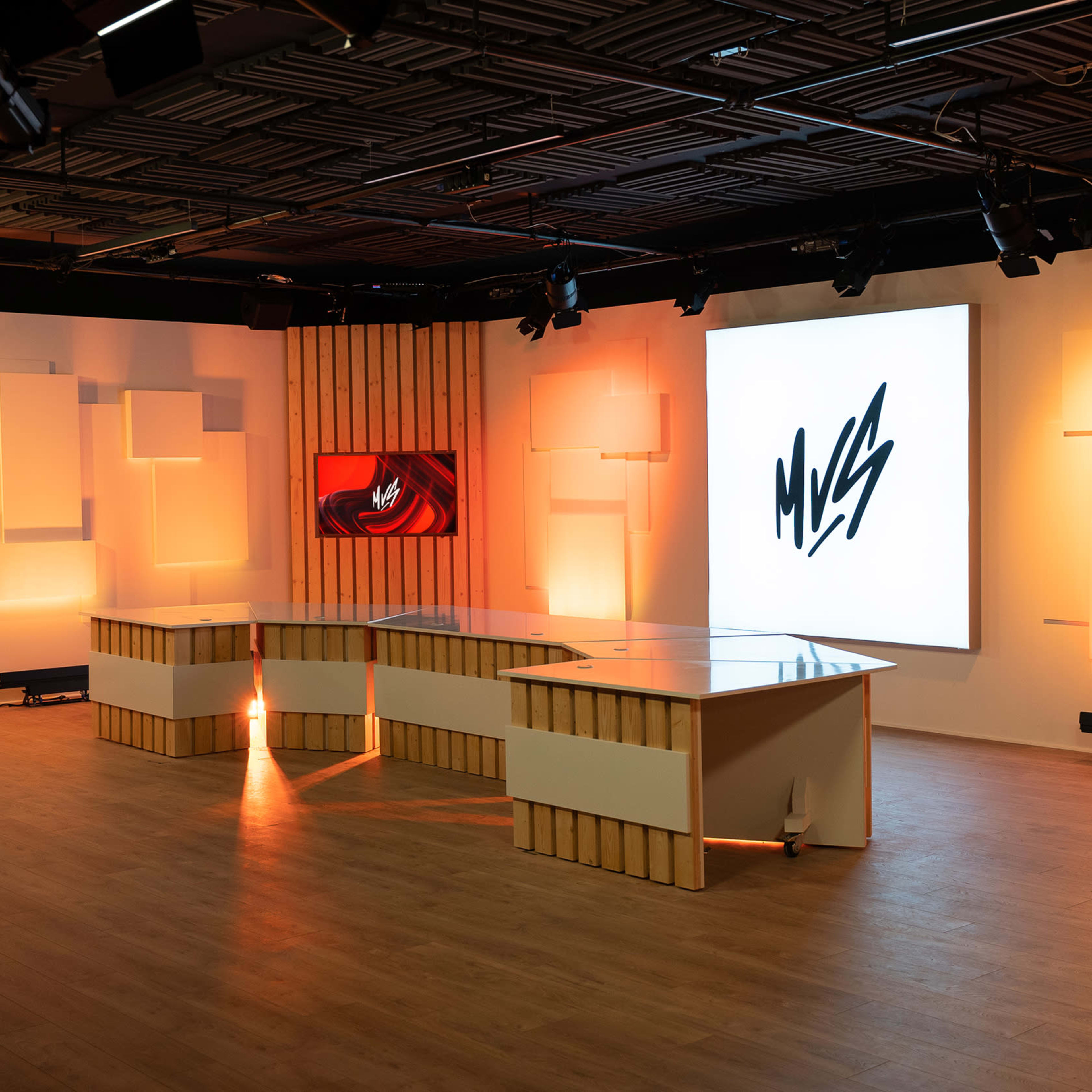 A modern studio setup with a central table and large screens displaying graphics, illuminated by soft orange lighting.