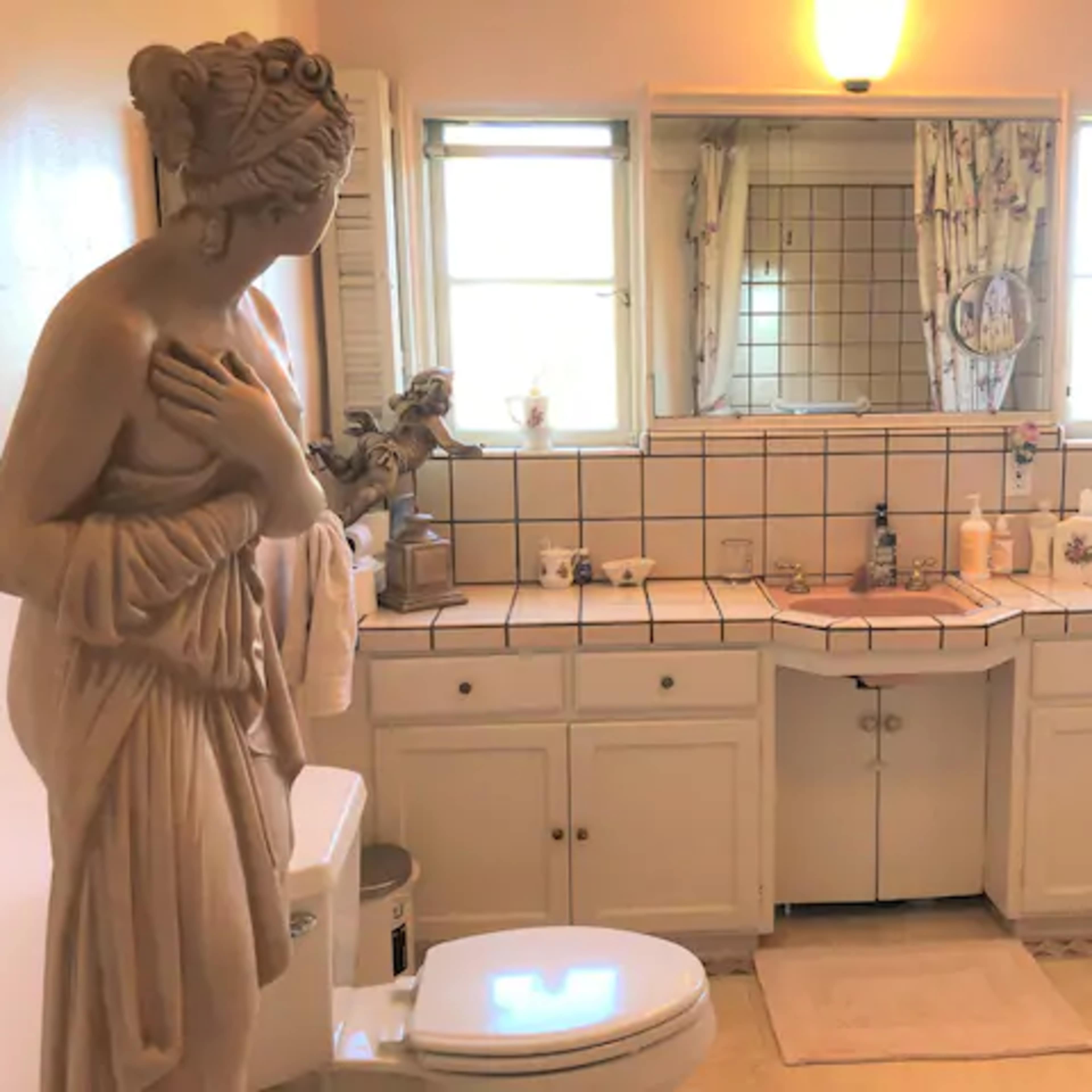 A bathroom features a large statue, a double vanity with a mirror, and light-colored tile flooring.