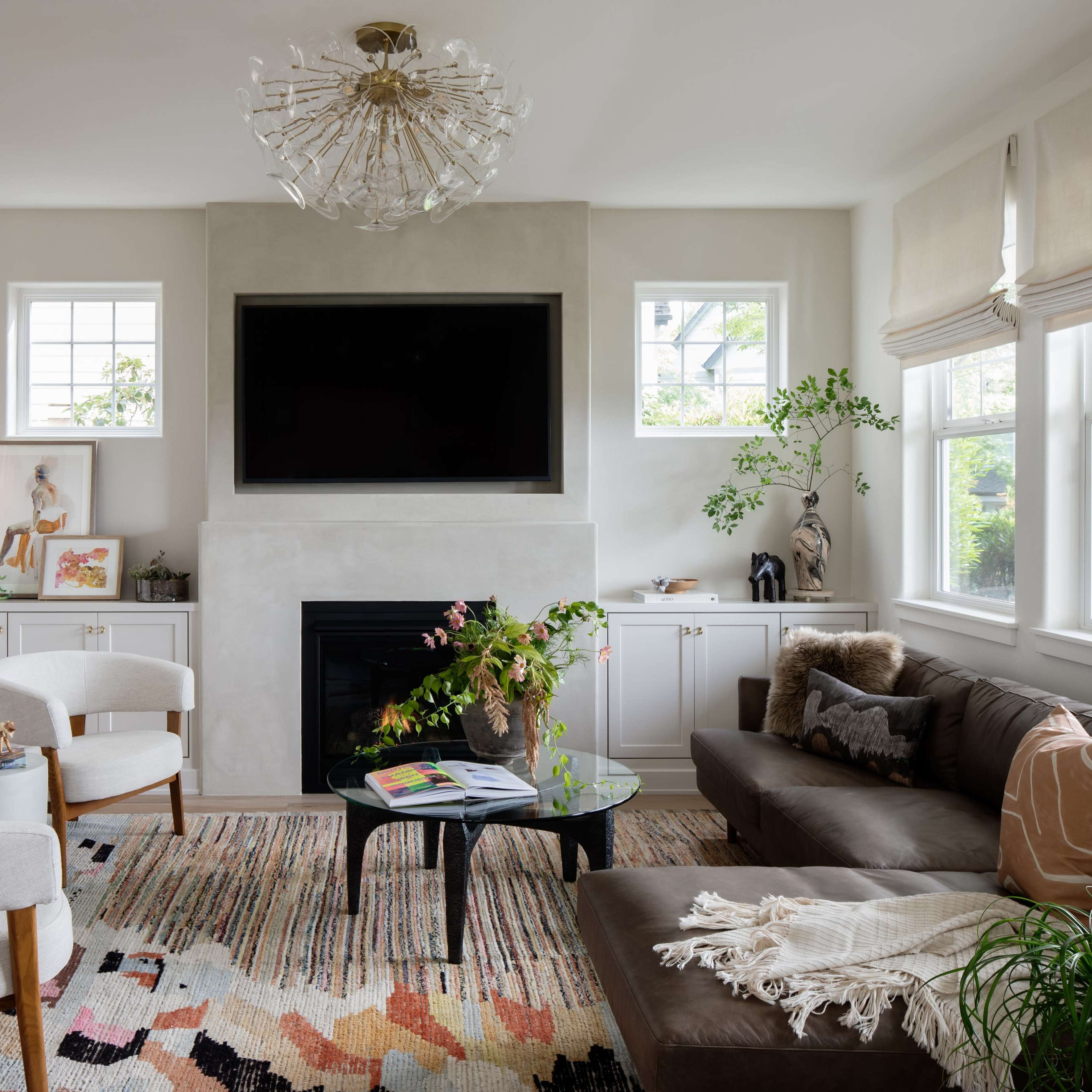 A modern living room features a dark leather sofa, a glass coffee table on a colorful rug, and a sleek fireplace with a mounted television above it.