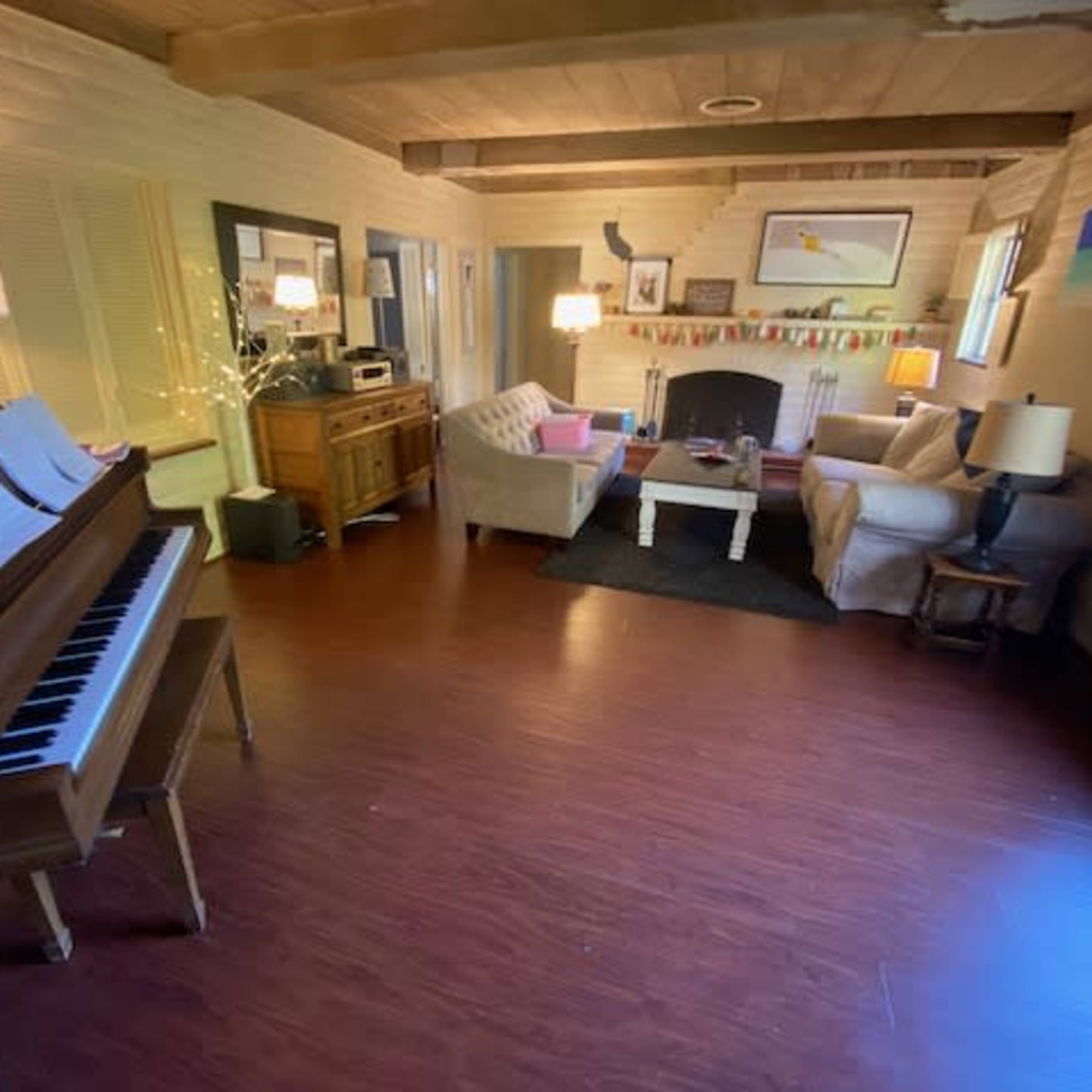 A living room with a piano, a sofa, a coffee table, a fireplace, and a wooden sideboard, all arranged around a dark area rug.