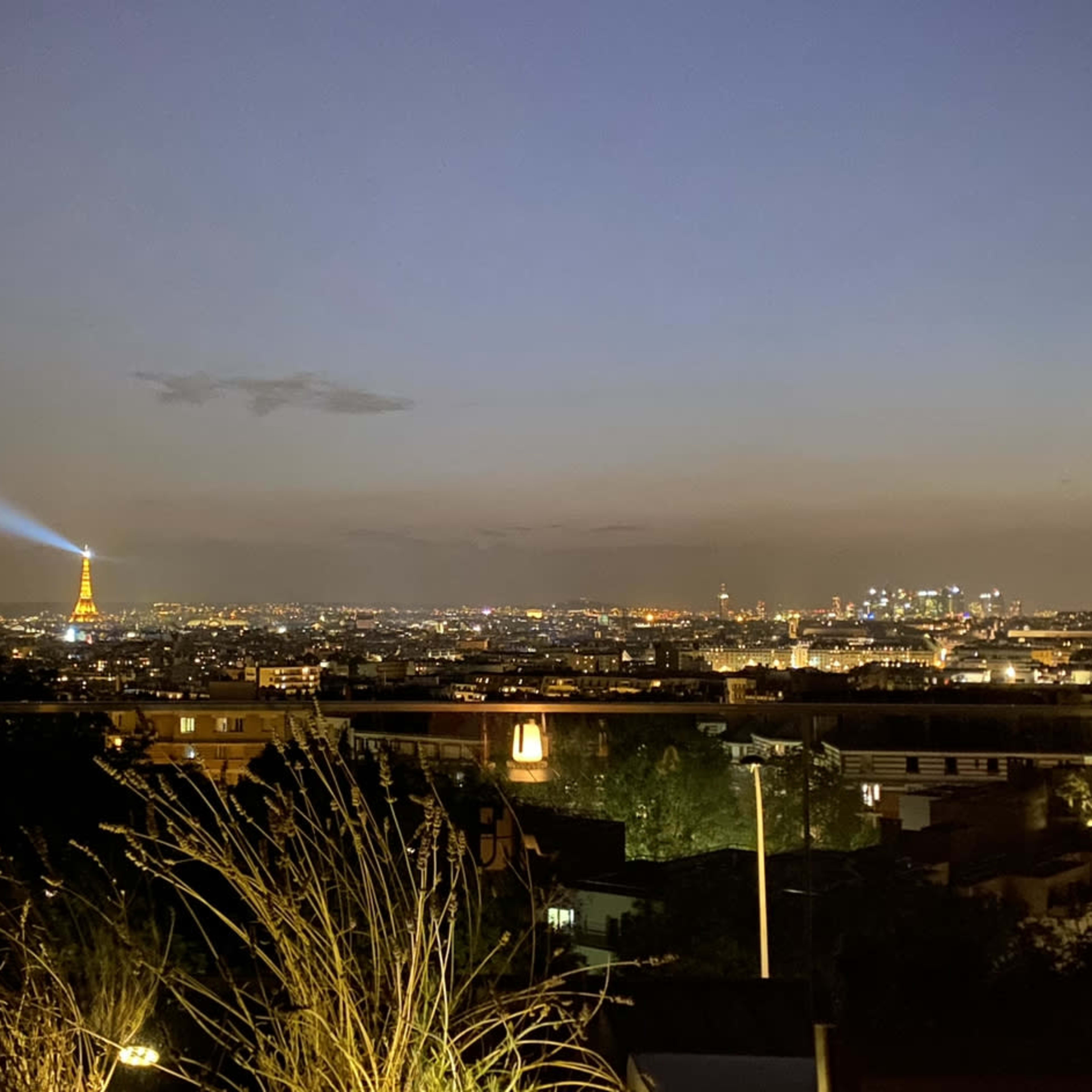 A night view of Paris with the Eiffel Tower illuminated and a beam of light projected into the sky.