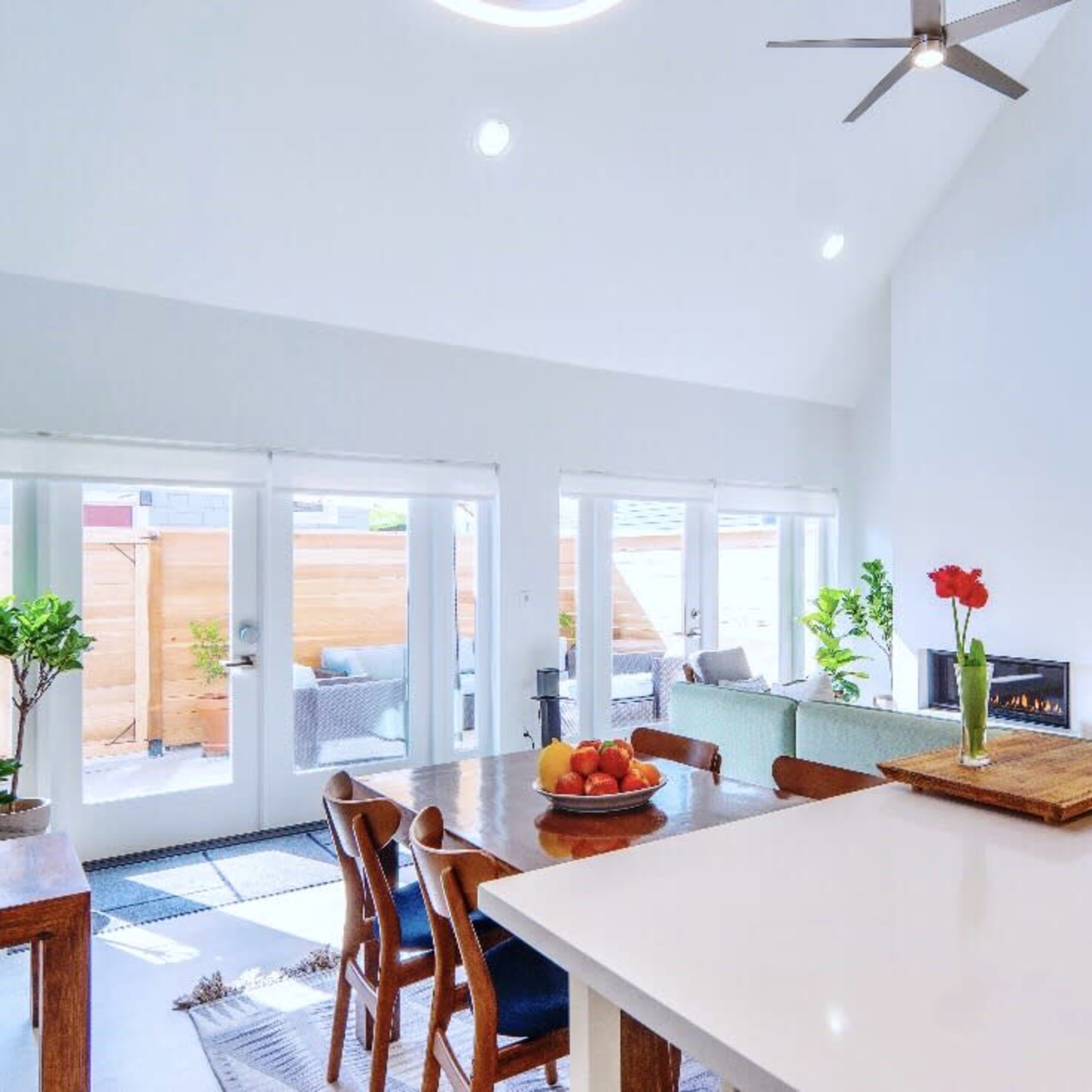 A modern open-concept living space features a dining area with a wooden table, a kitchen island, and large windows illuminating the room.