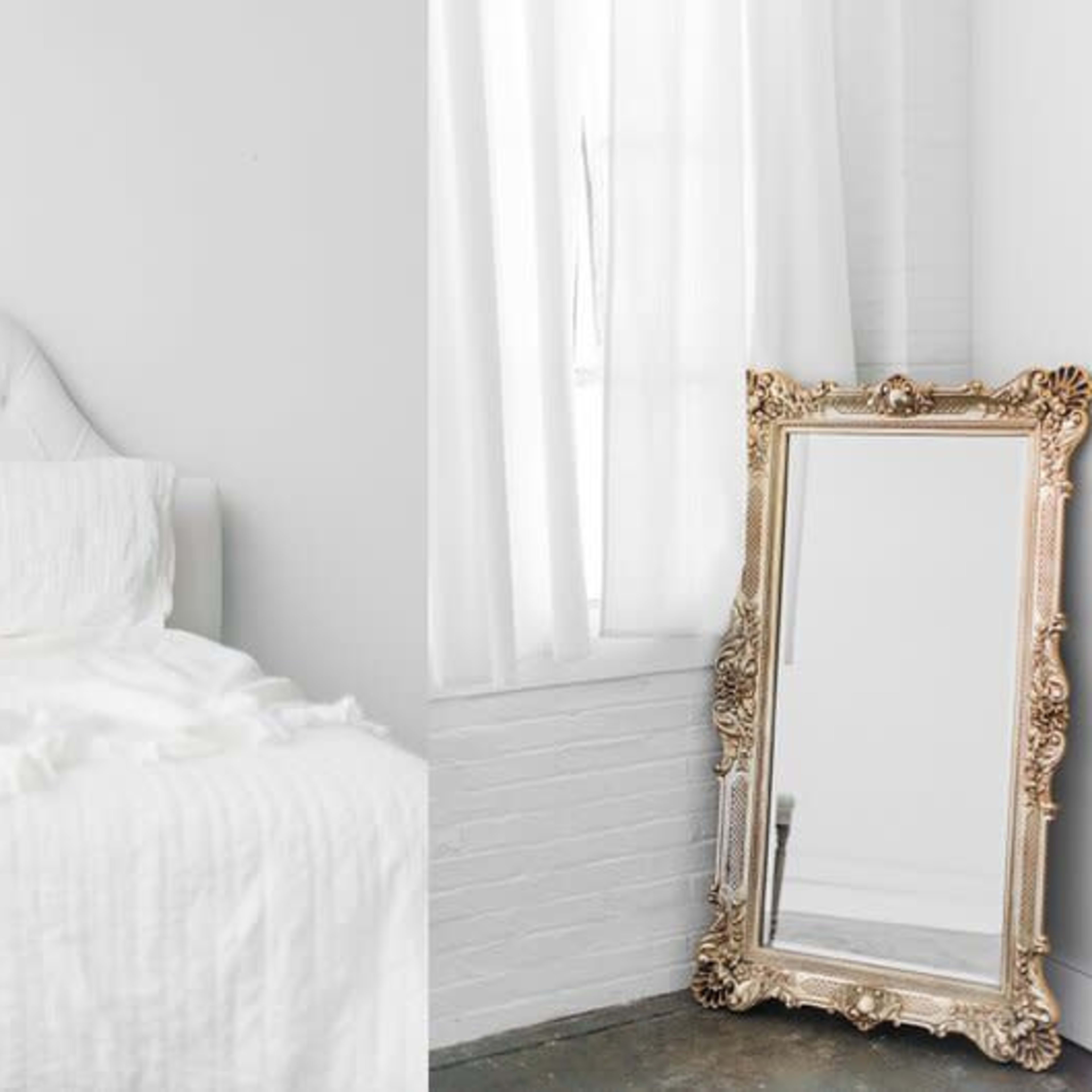 A bright bedroom features a white bed with light linens and a large, ornate mirror against the wall.
