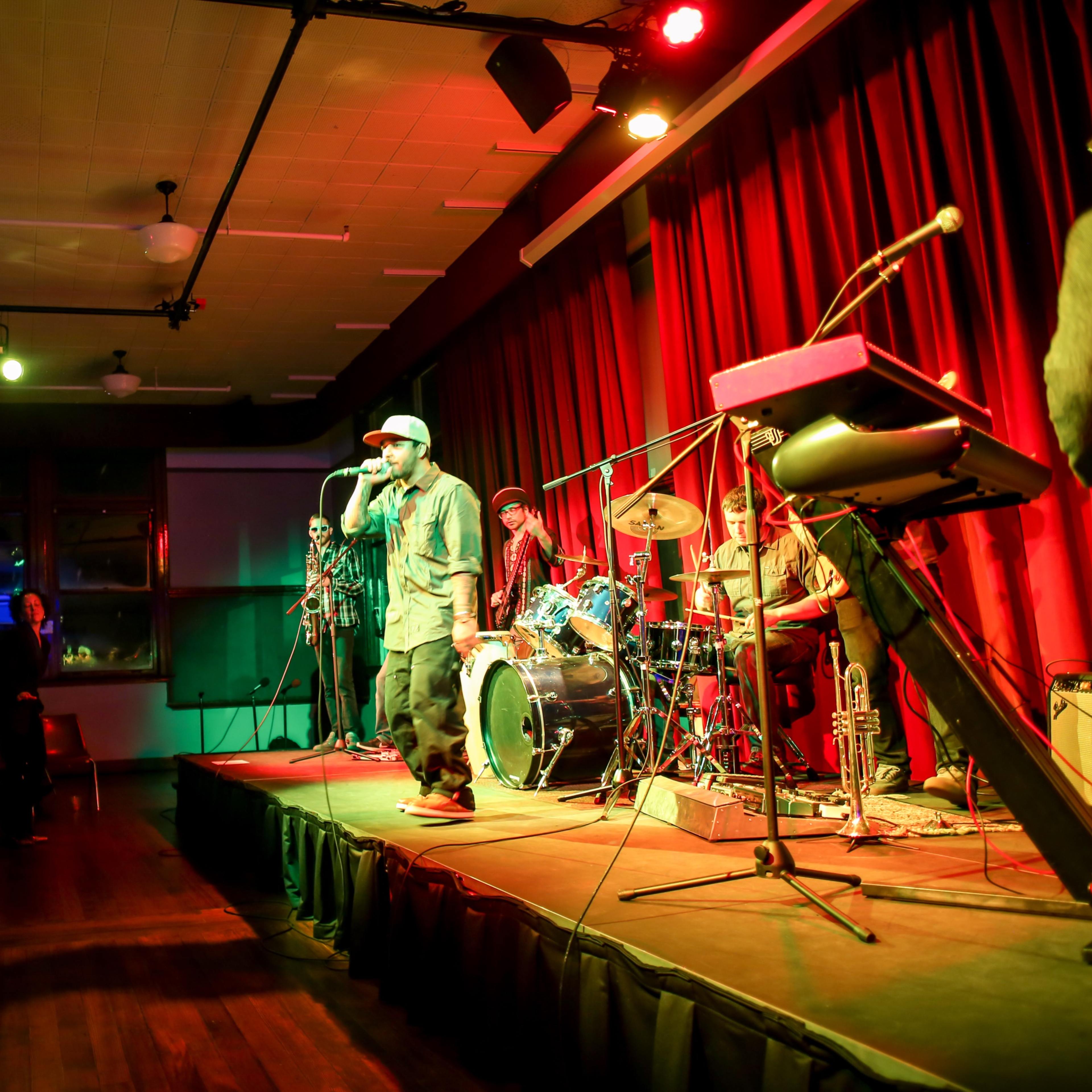 A performer raps on stage while a band plays behind him and an audience watches from below.
