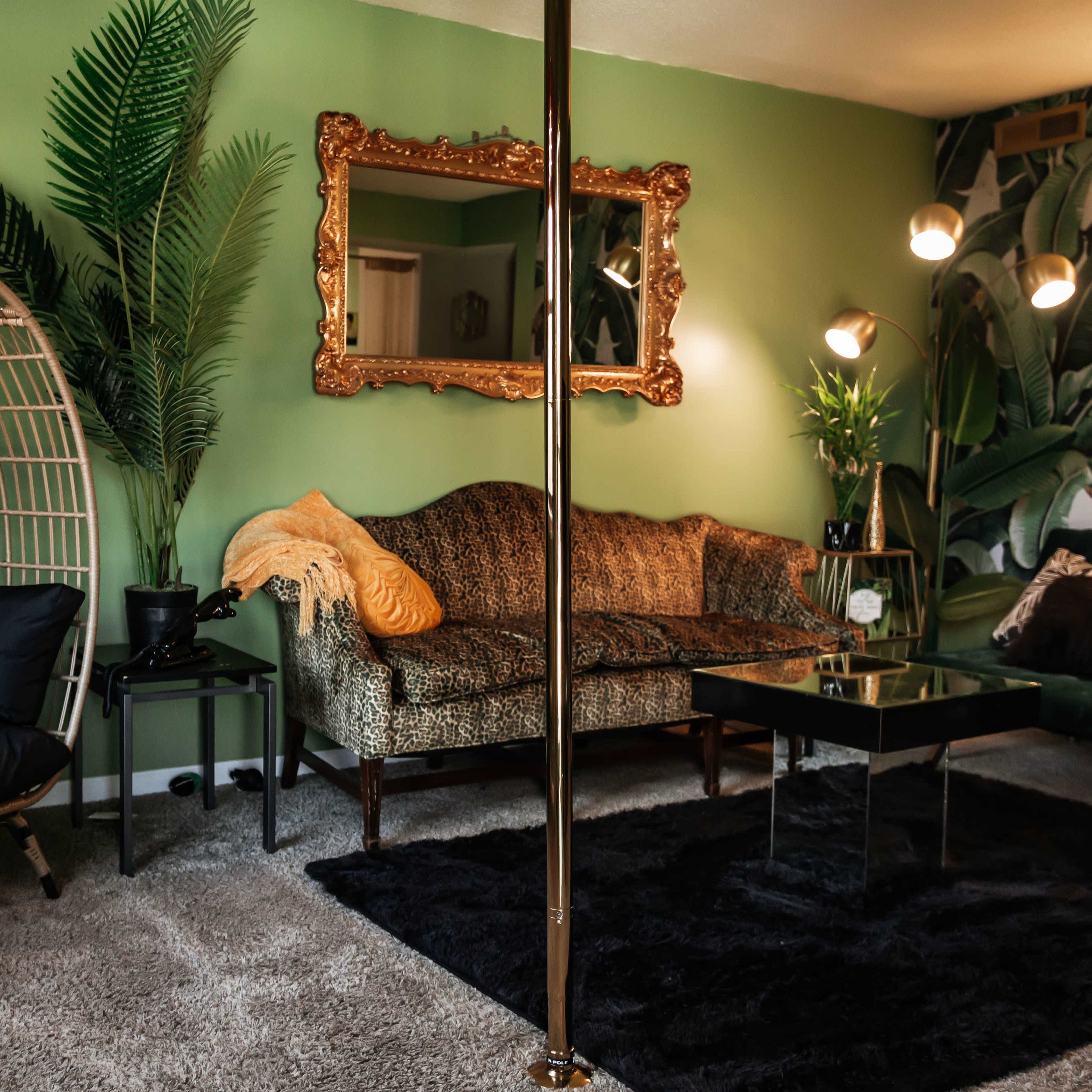 A stylish living room featuring a green wall, a retro-style sofa, a gold-framed mirror, and a tall plant alongside a modern black coffee table.