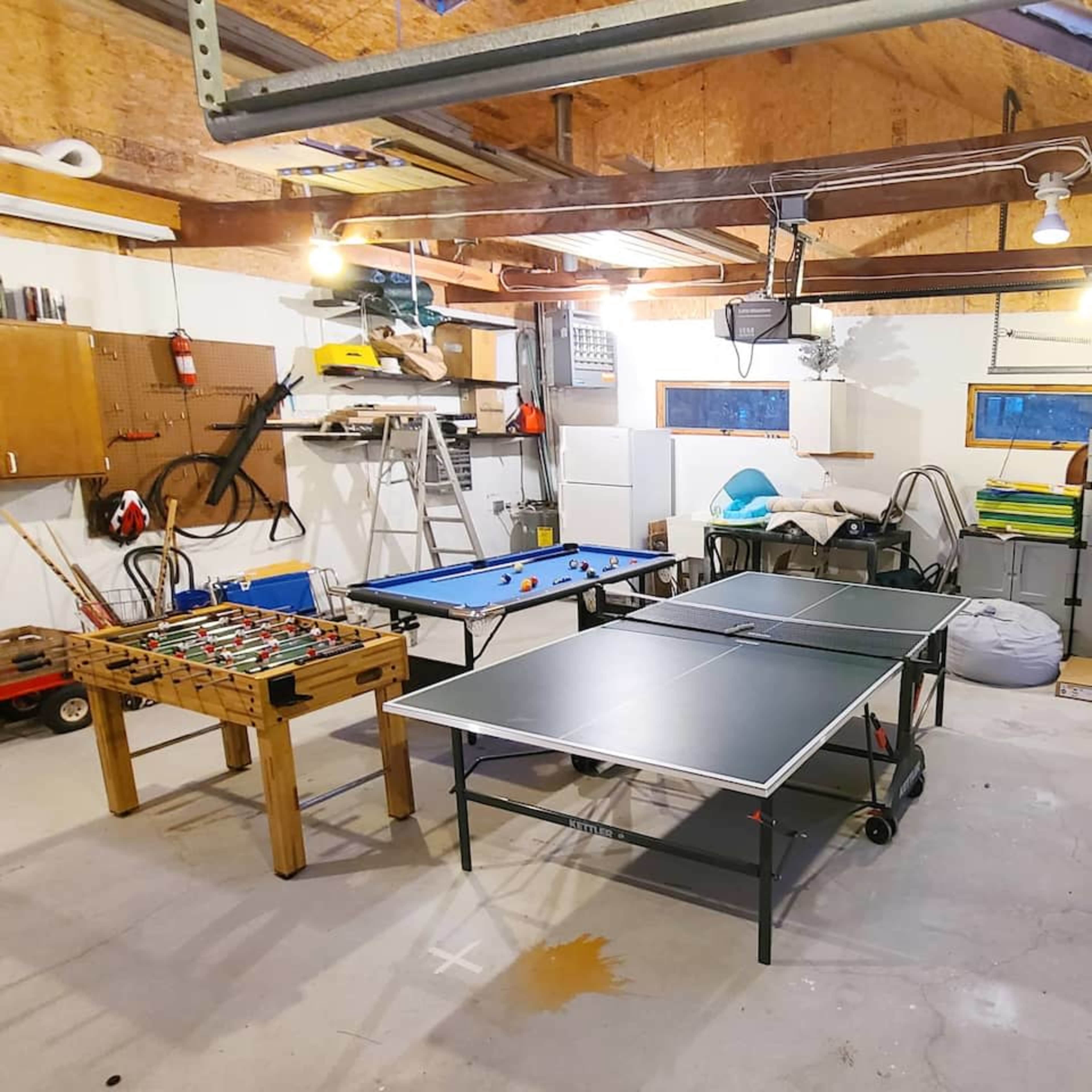 The garage features a table tennis table, a foosball table, and various storage units along with a ladder and exercise equipment.