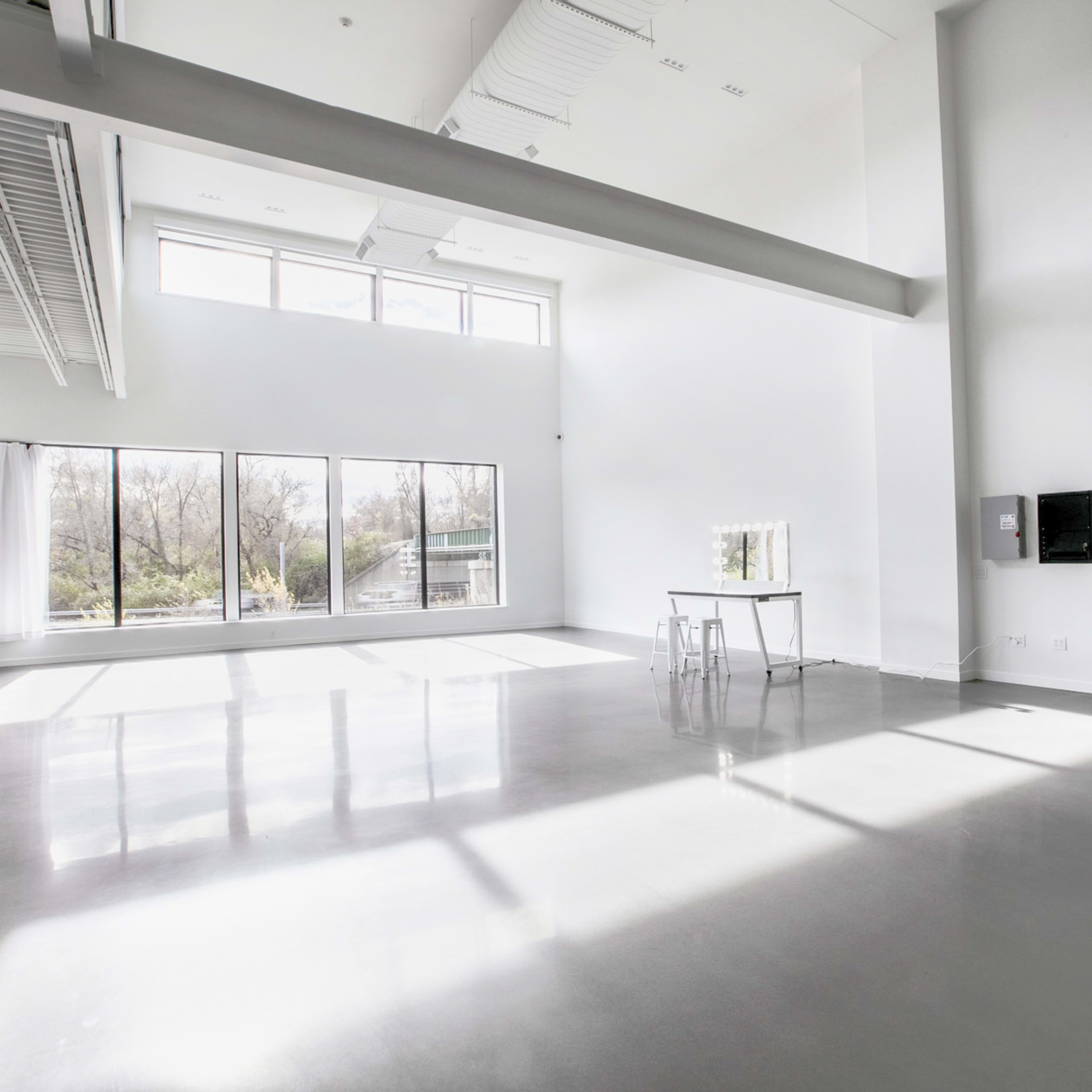 A spacious, empty room with large windows allowing natural light to illuminate the polished concrete floor and minimal furnishings.