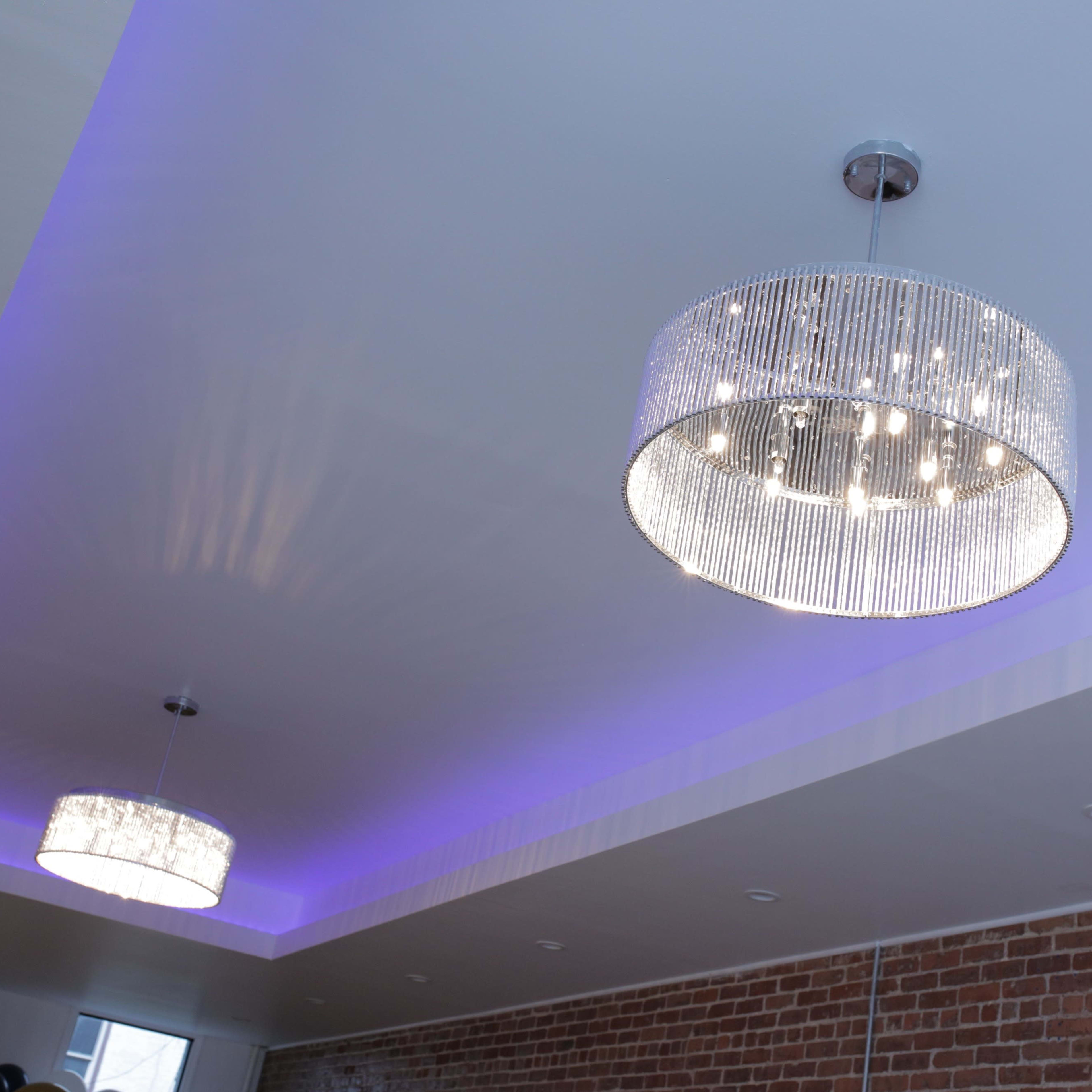 Two circular crystal chandeliers hanging from a ceiling with a purple LED light strip and exposed brick walls.