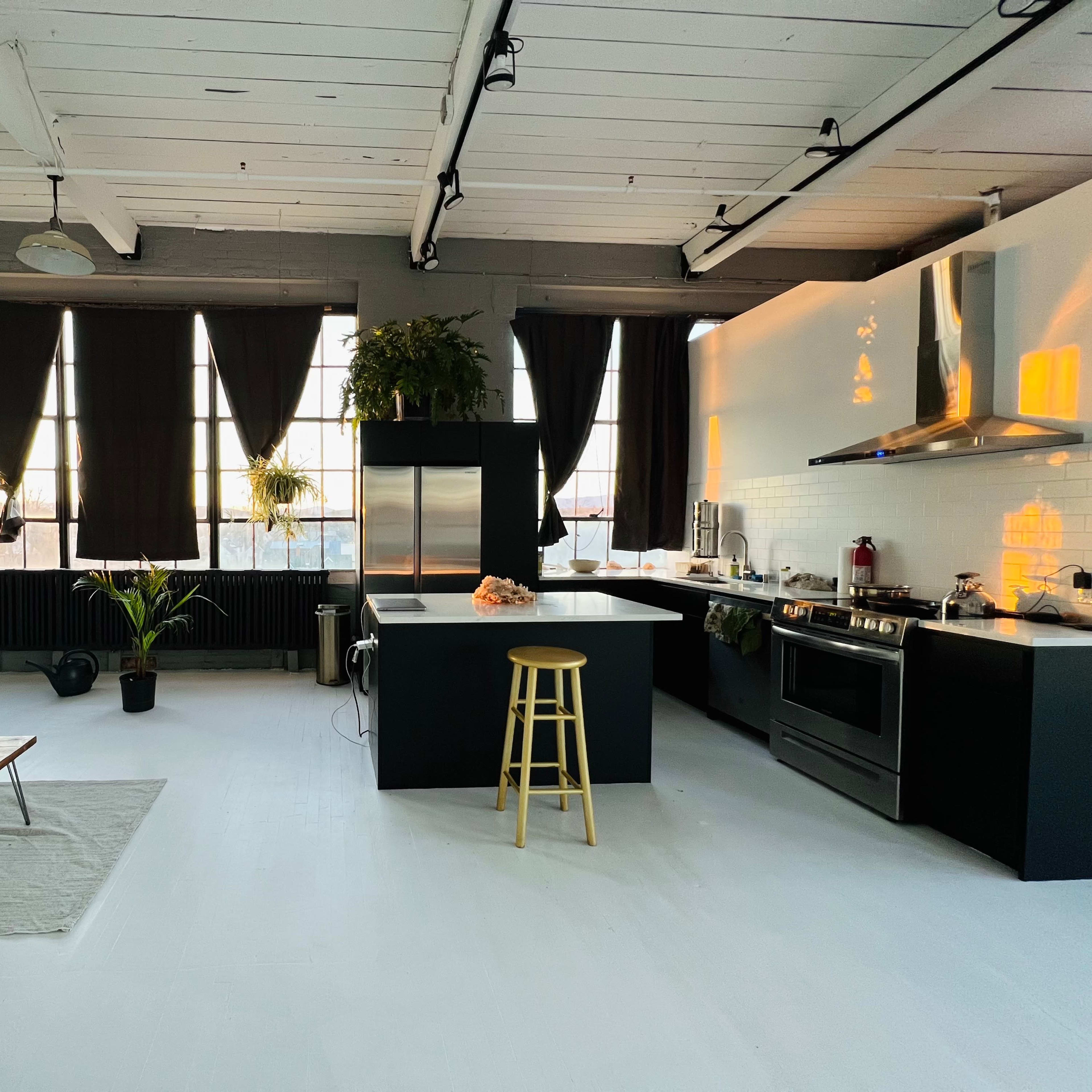 A modern kitchen with black cabinetry, a central island, and large windows allowing natural light to illuminate the space.