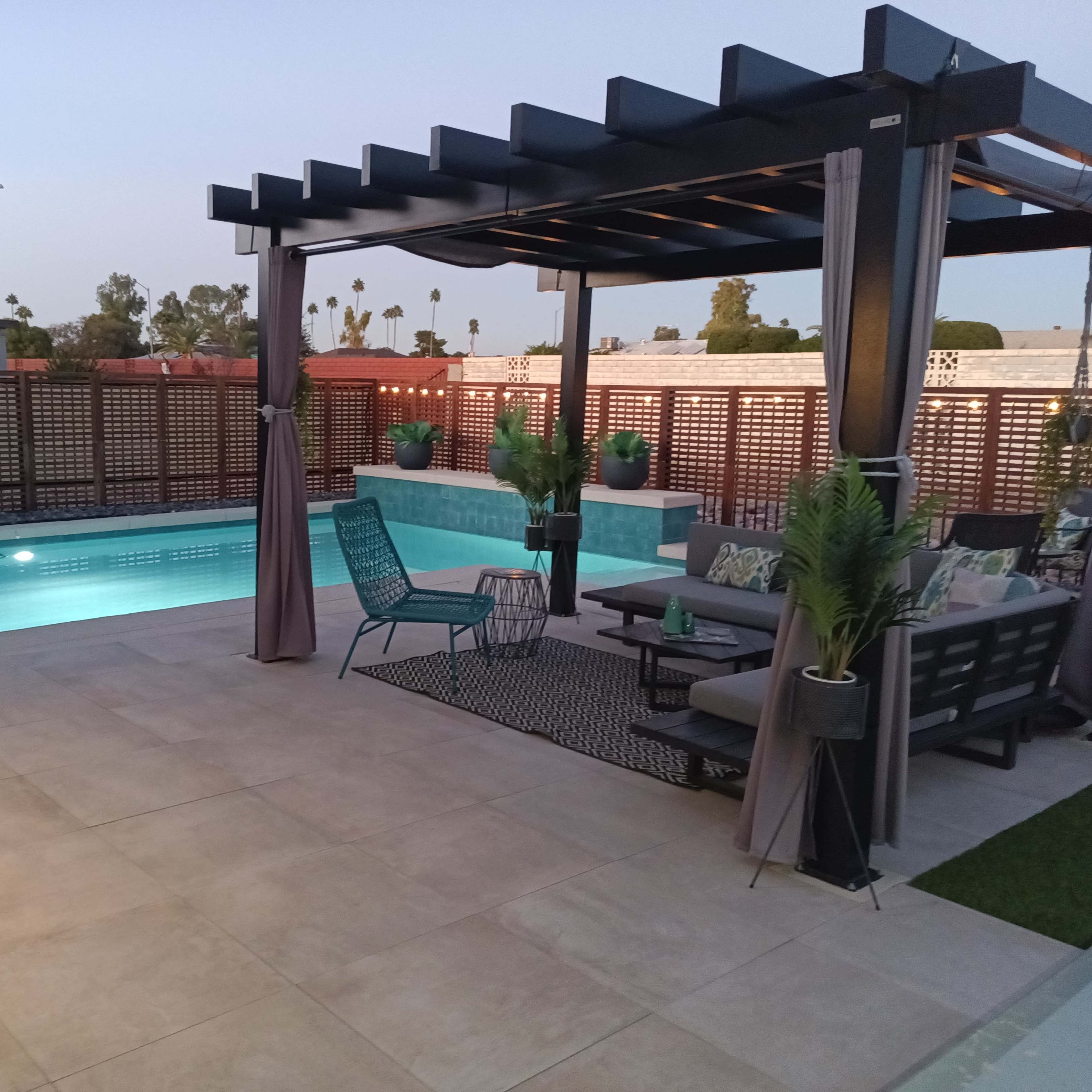 A modern outdoor space featuring a pool, a pergola with seating, and surrounding landscaping.