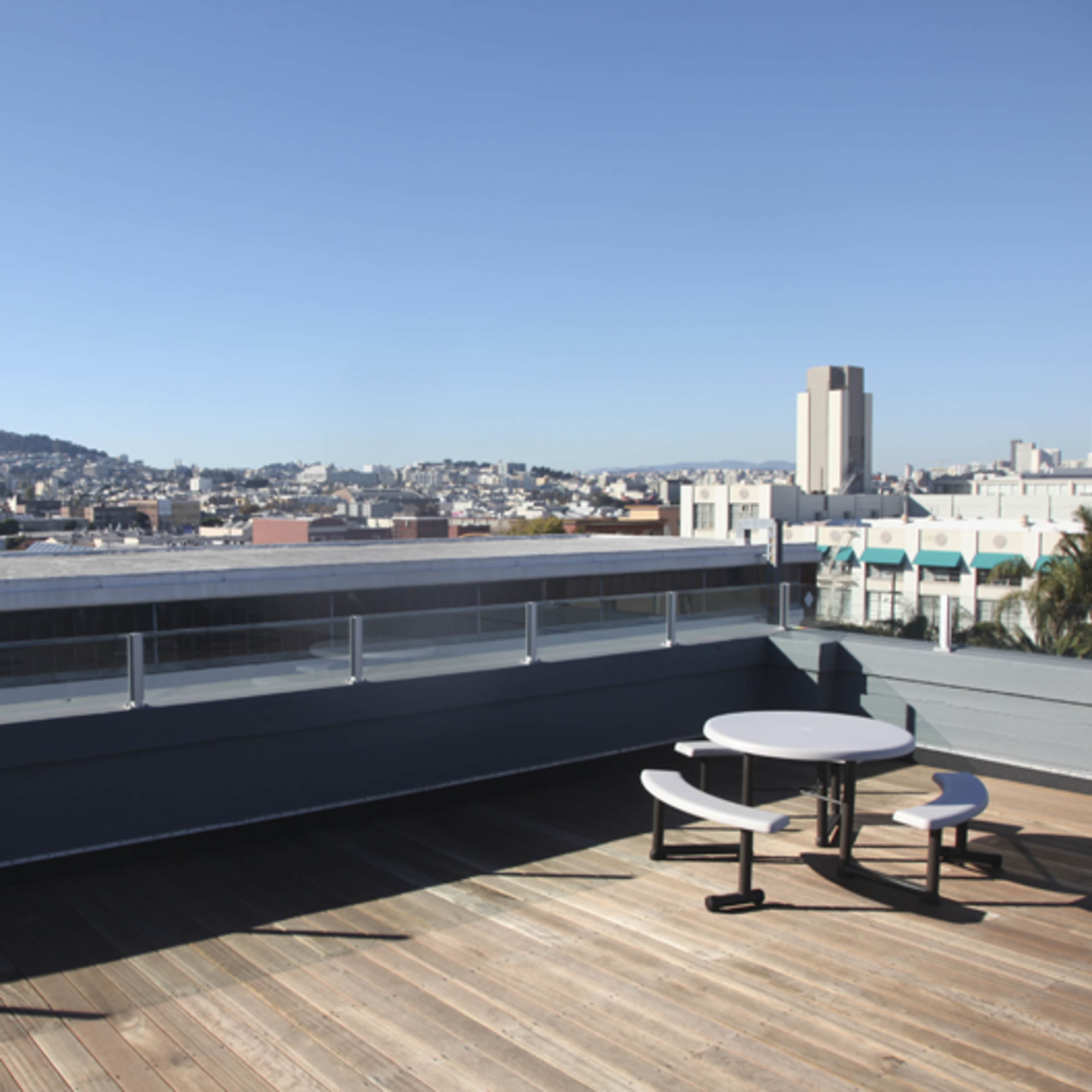 A rooftop terrace features a circular table and two chairs overlooking a cityscape with distant hills.