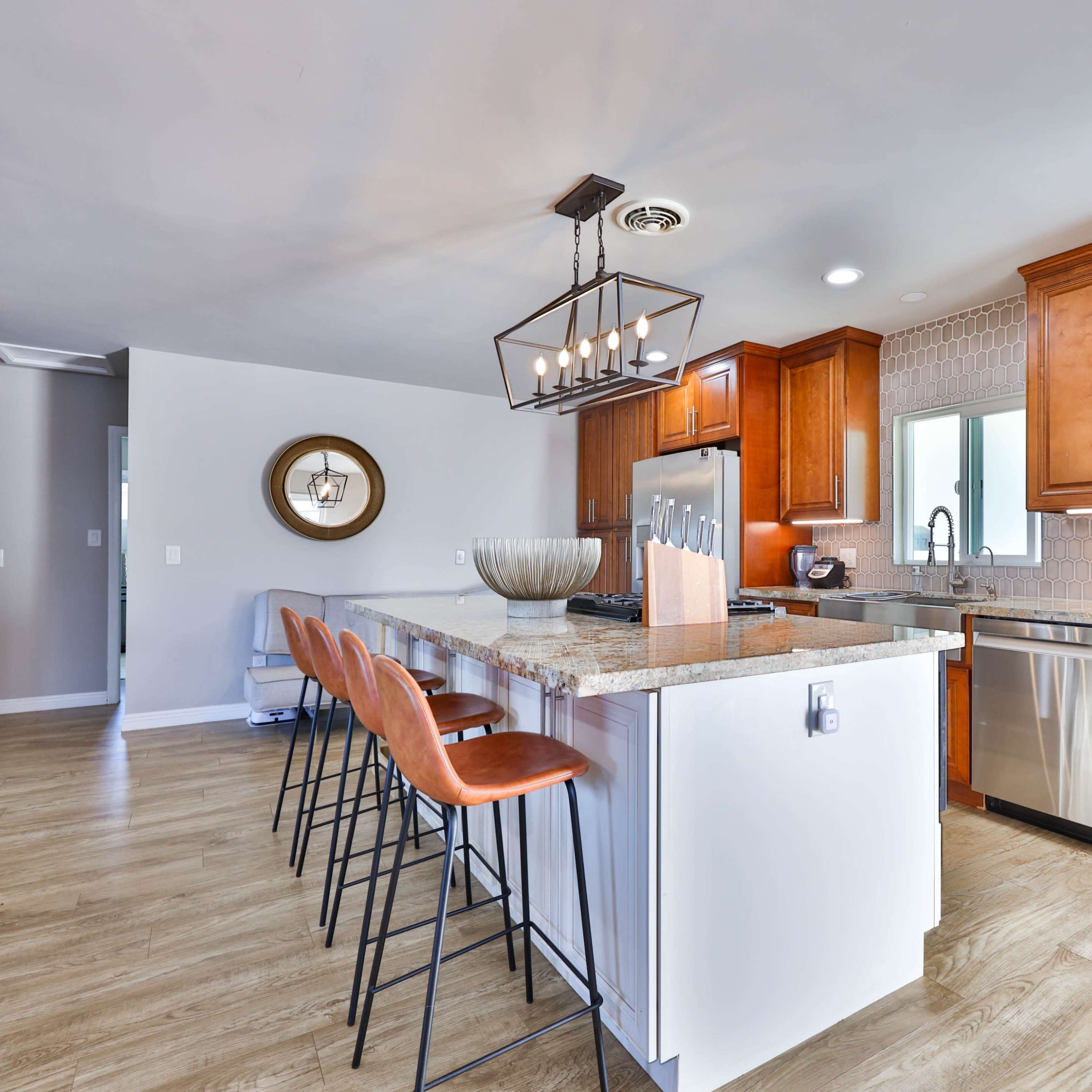 A modern kitchen features wooden cabinets, a large island with bar stools, and stainless steel appliances.