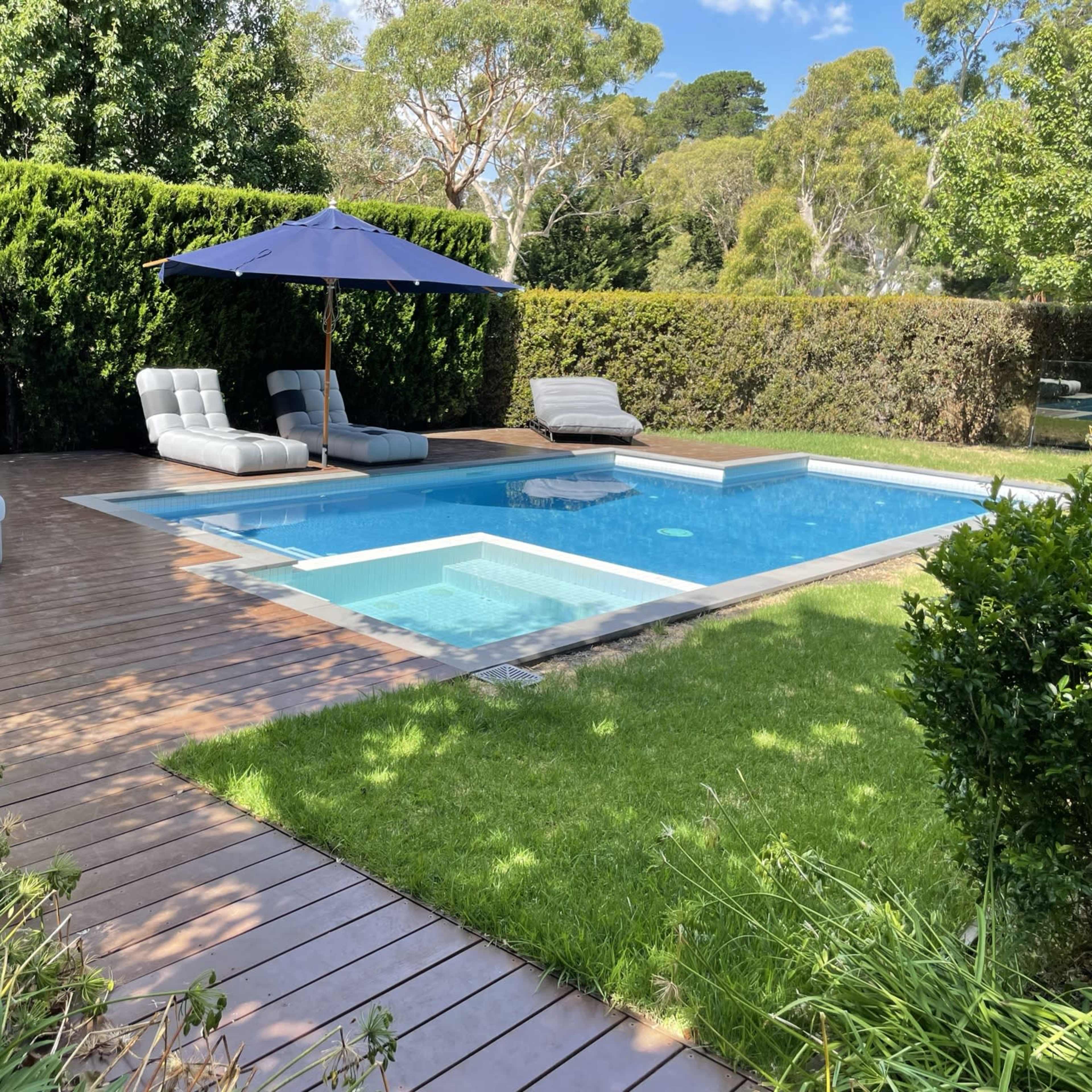 A well-maintained backyard features a swimming pool surrounded by sun loungers and an umbrella, with grass and wooden decking nearby.