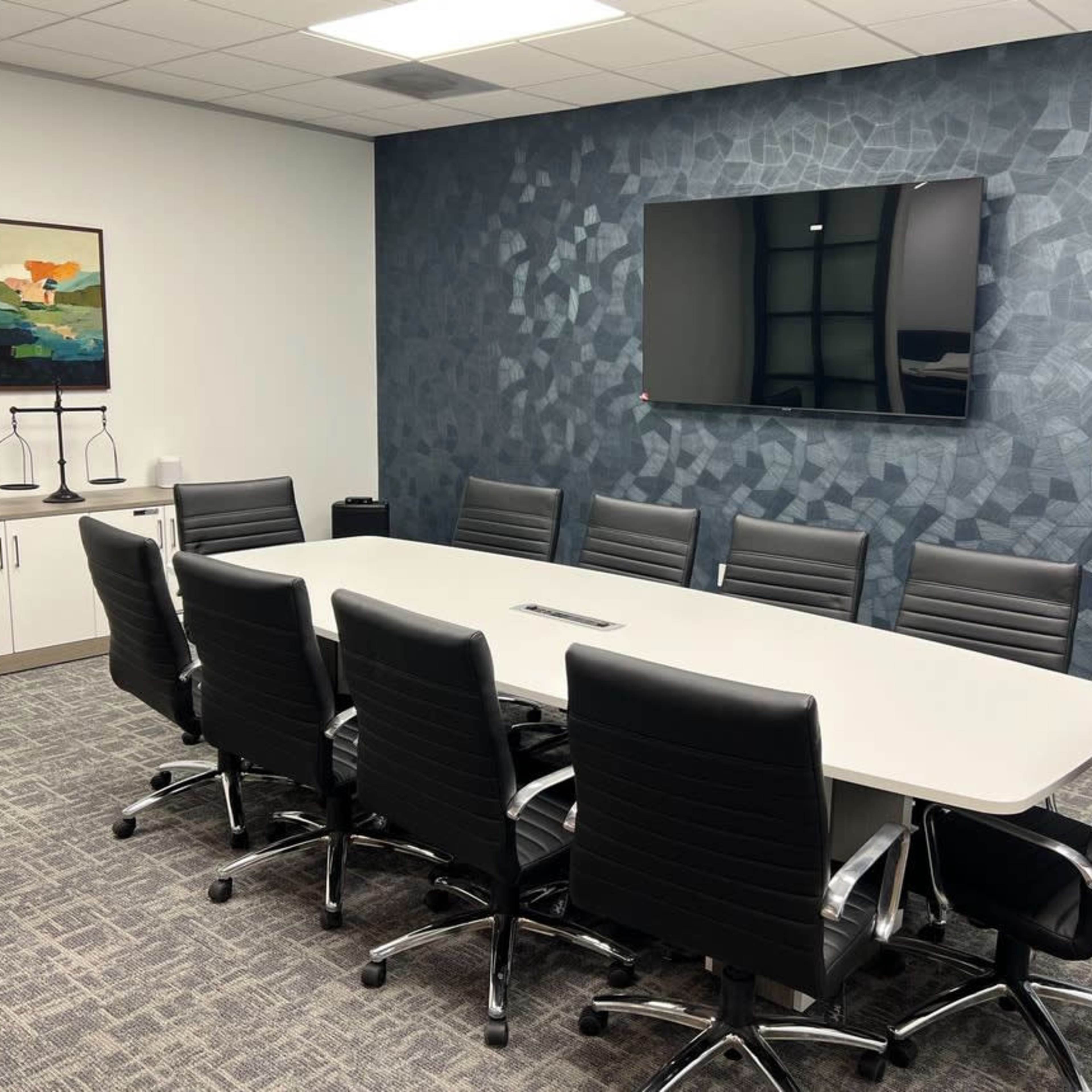 A modern conference room with a long table surrounded by black chairs, a television mounted on the wall, and a large abstract painting.