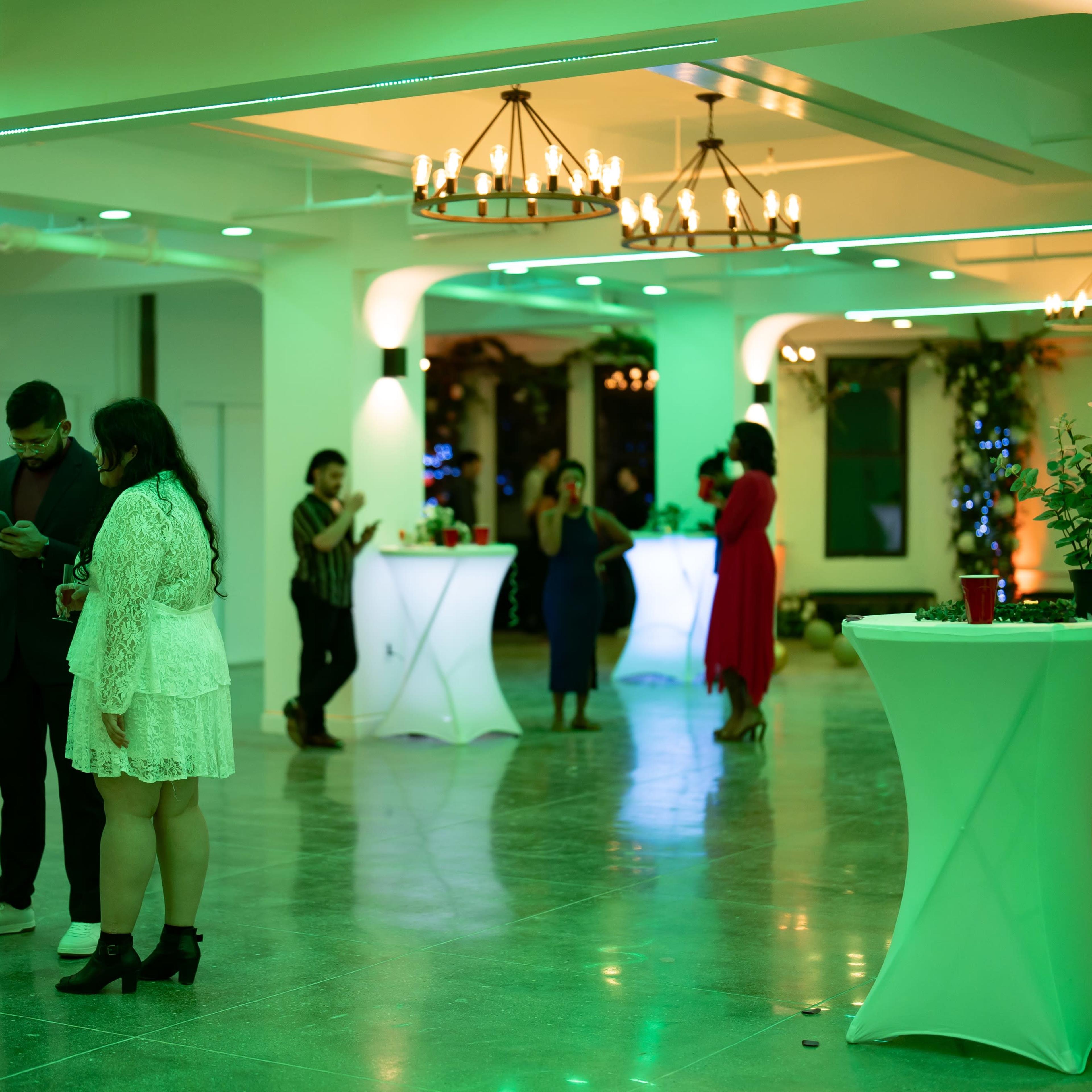 A group of people socialize at a modern event space decorated with green lighting and high-top tables.