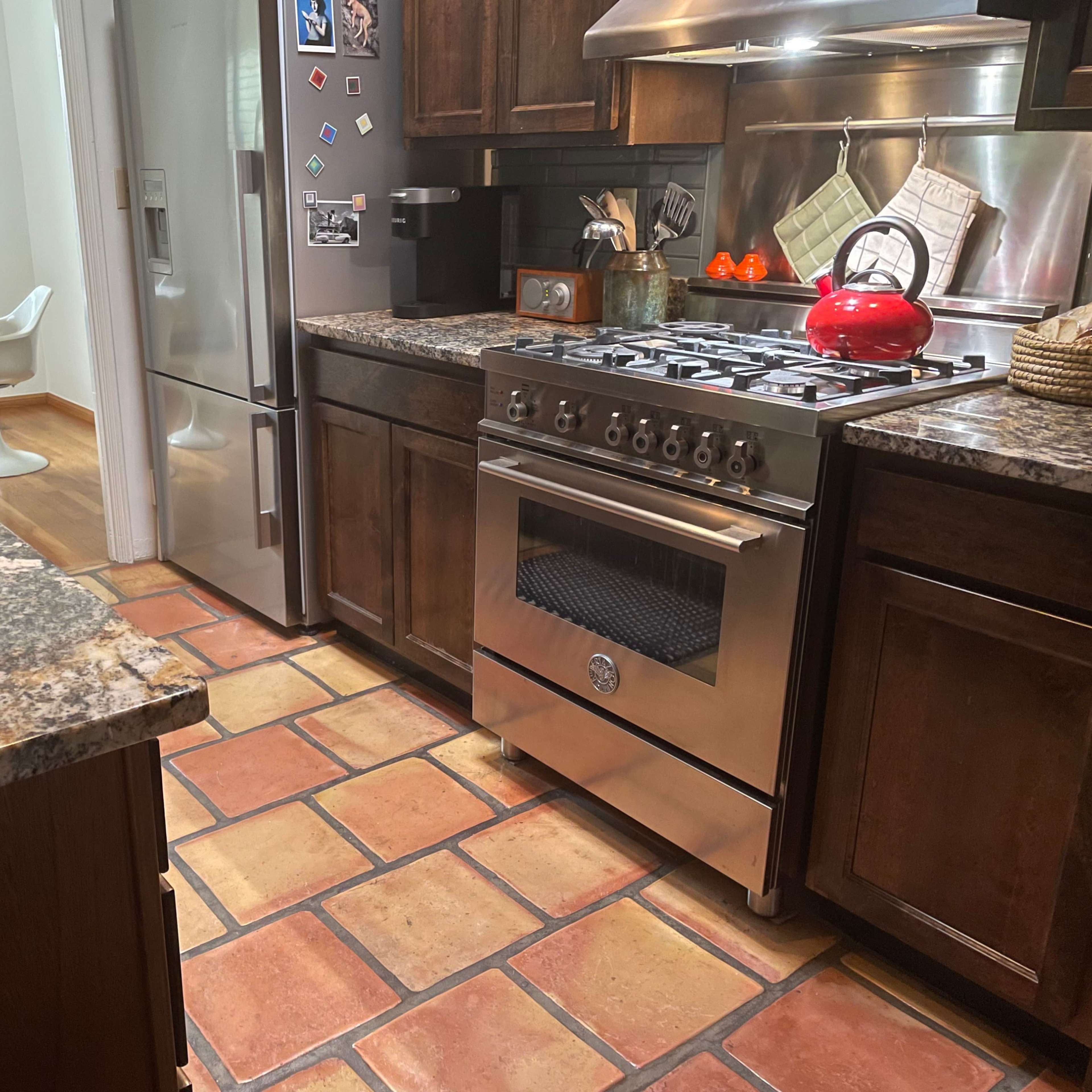 The kitchen features granite countertops, a stainless steel stove, a red kettle on the stove, and tiled flooring.