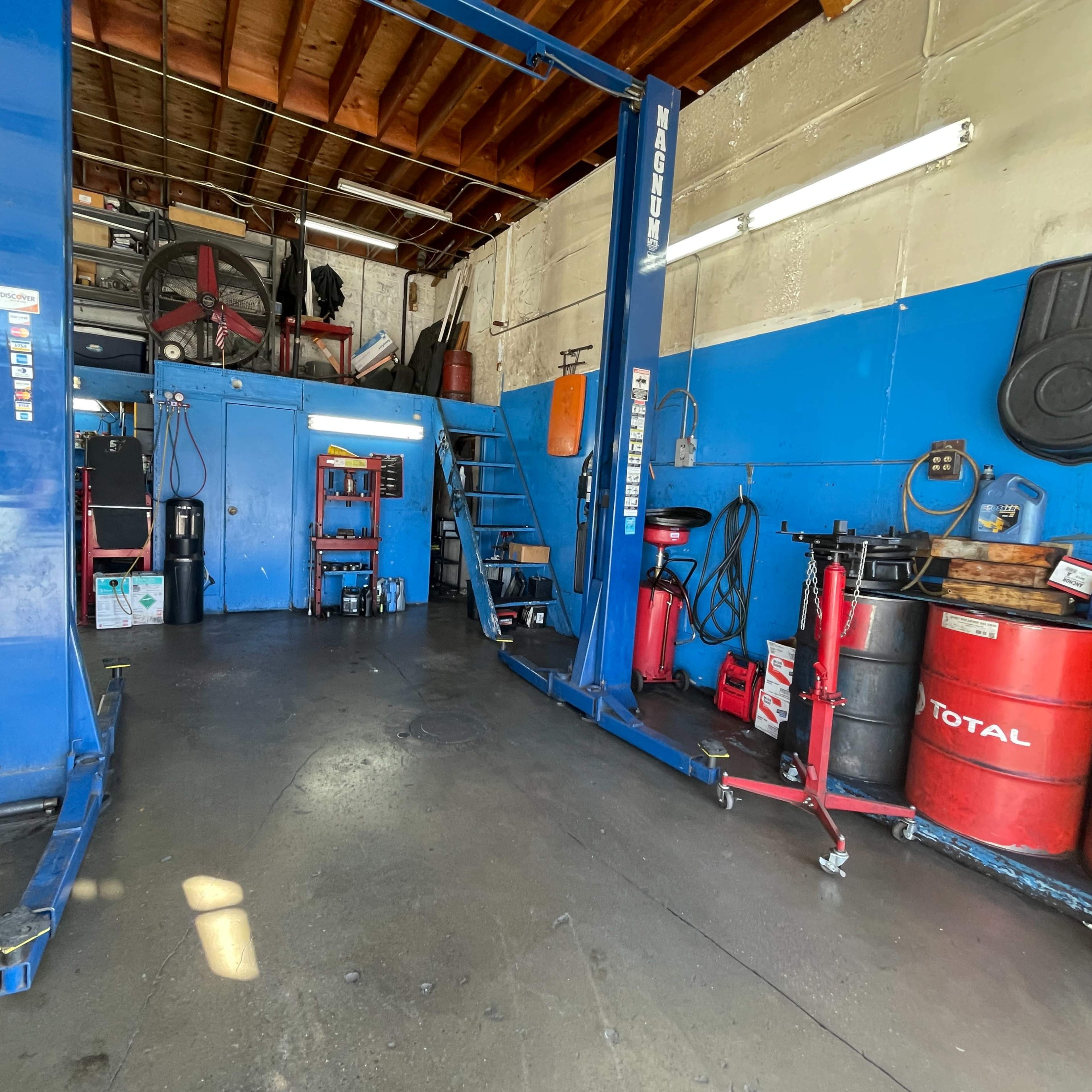 An auto repair shop interior featuring a car lift, tool storage, and various equipment on the floor.