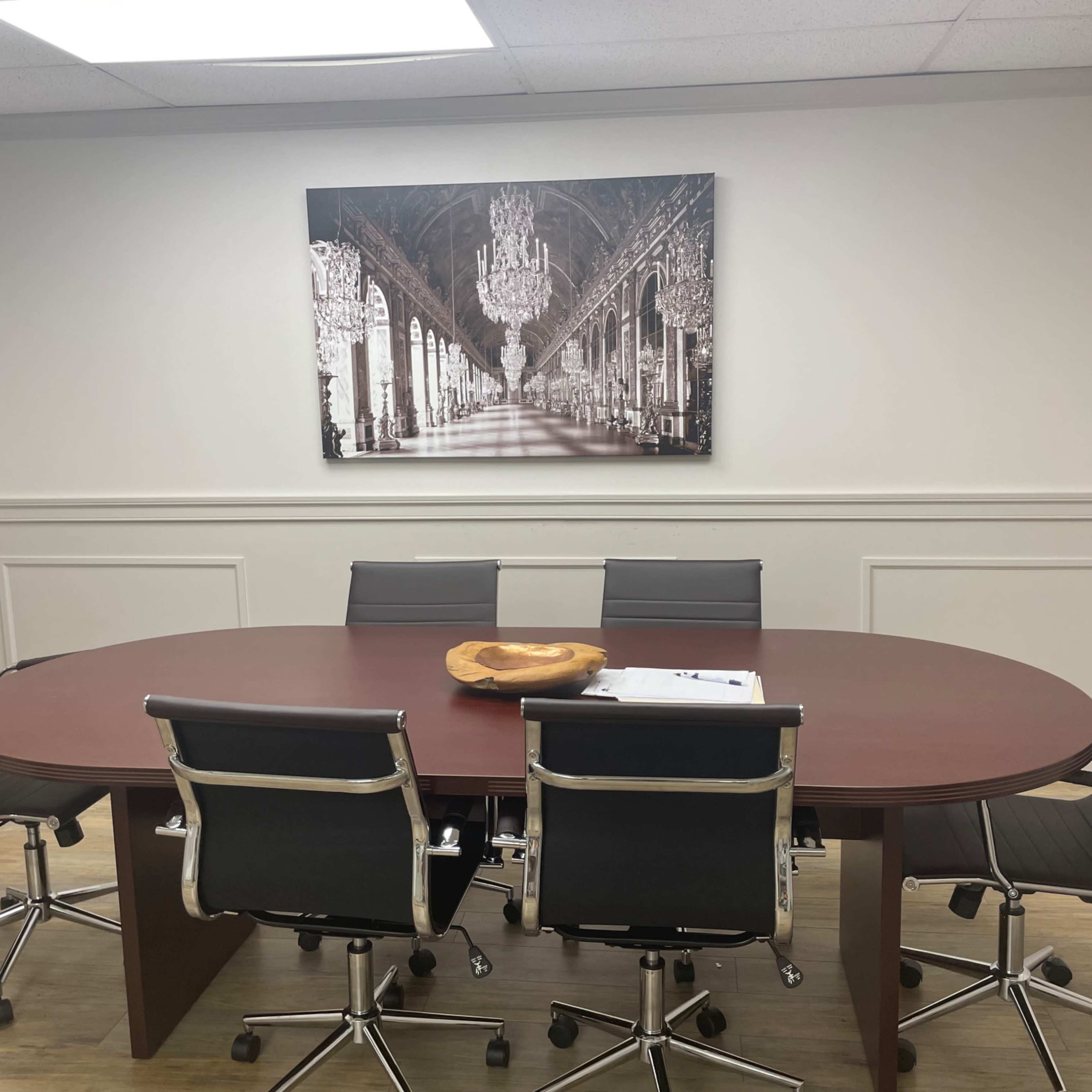A modern conference room with an oval table surrounded by six black chairs and a large framed black-and-white photograph on the wall.