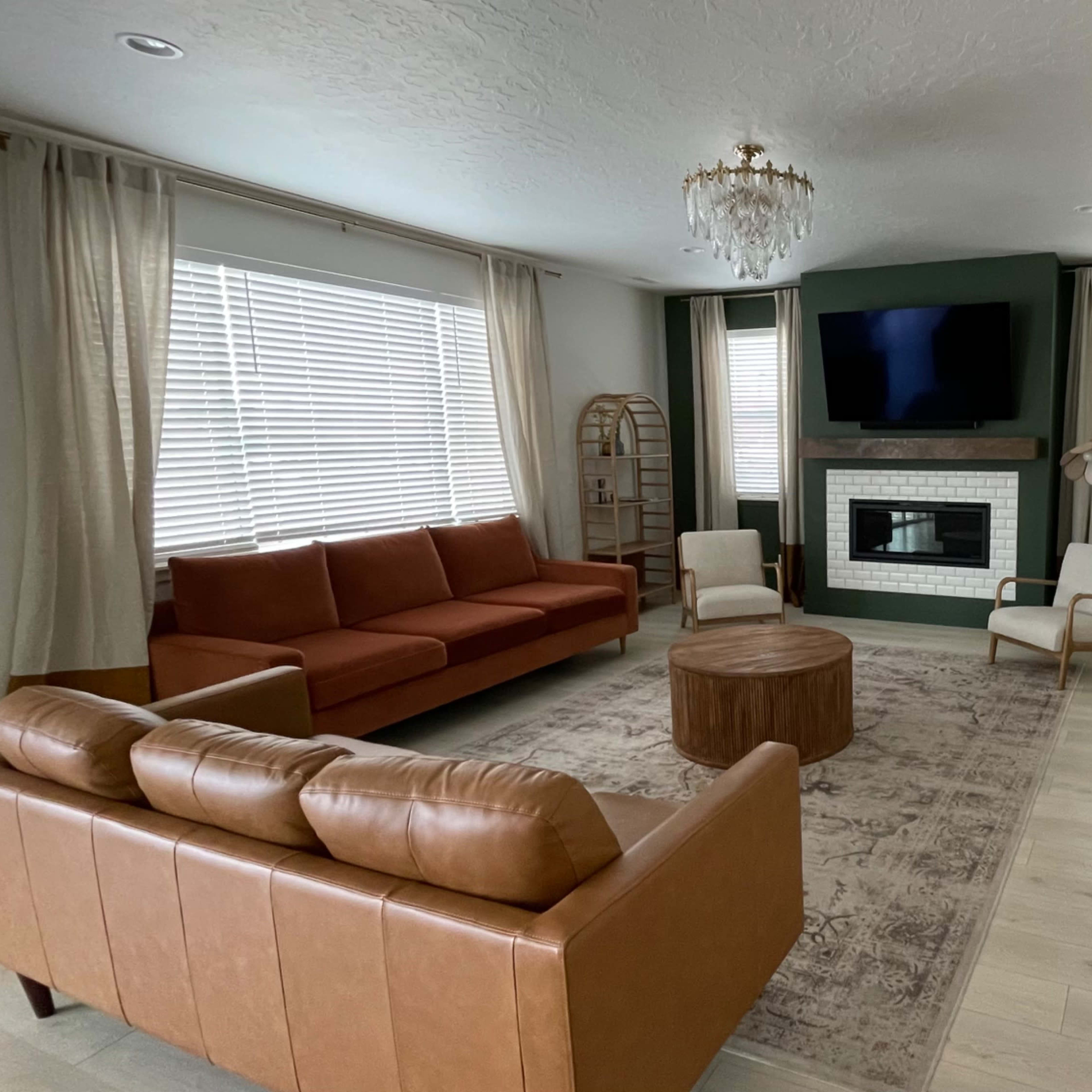 A modern living room features a brown leather sofa, a circular wooden coffee table, and a fireplace with a large television above it.