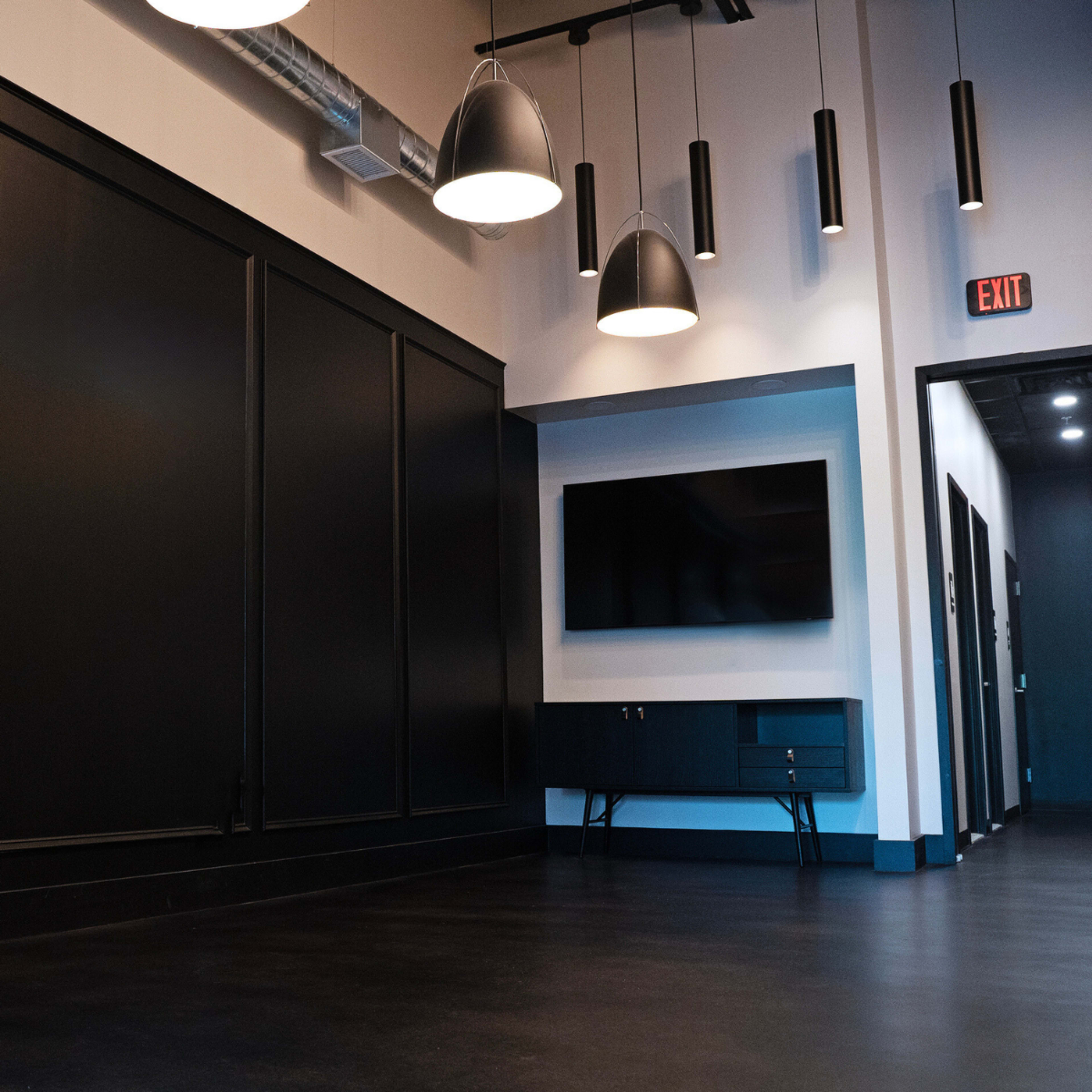 An interior space with black paneling, modern lighting fixtures hanging from the ceiling, and a wall-mounted television next to a console table.