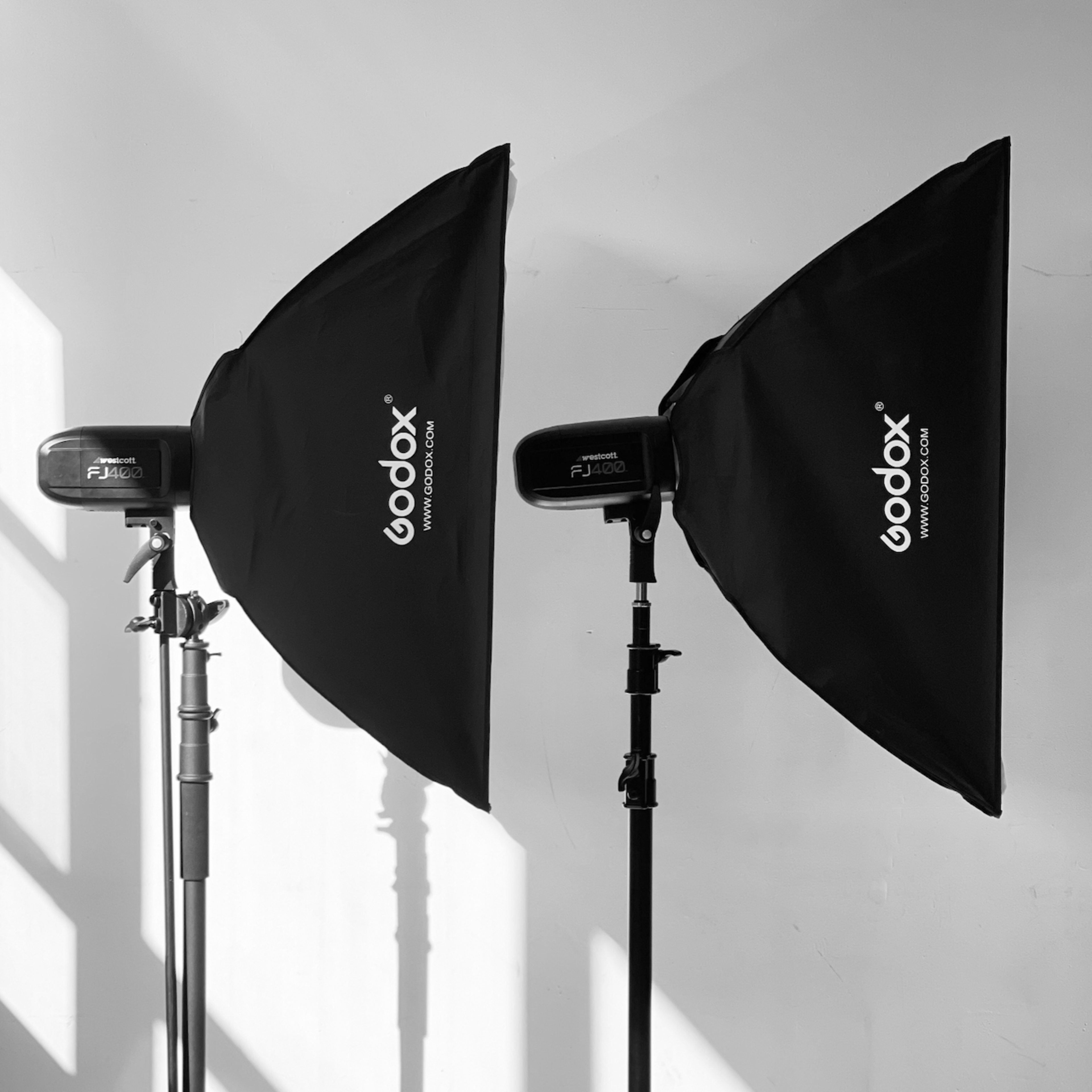 Two Godox studio light setups with softboxes are positioned against a white wall, casting shadows in the space.