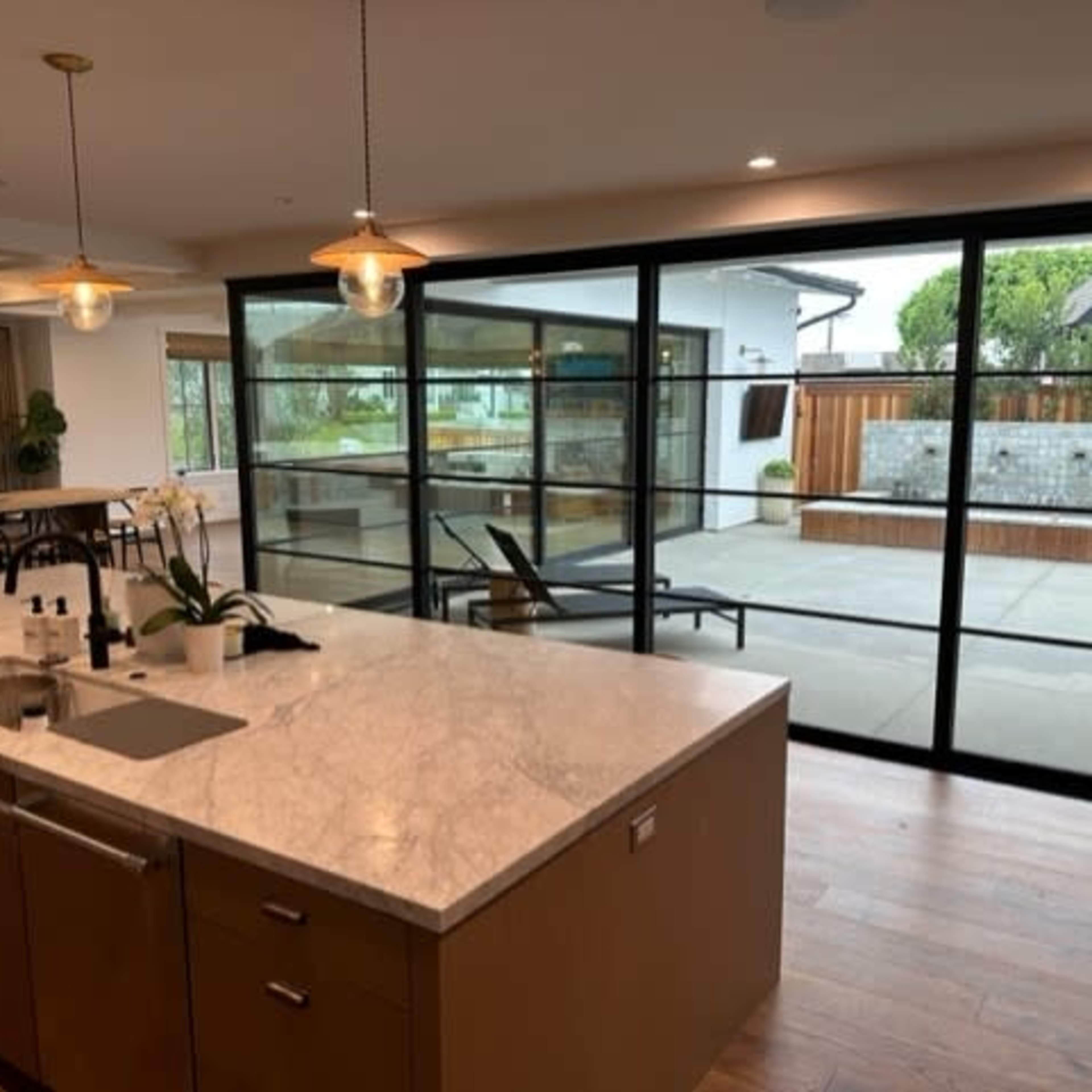 A modern kitchen with a marble countertop and an open view through large glass sliding doors to an outdoor patio area.