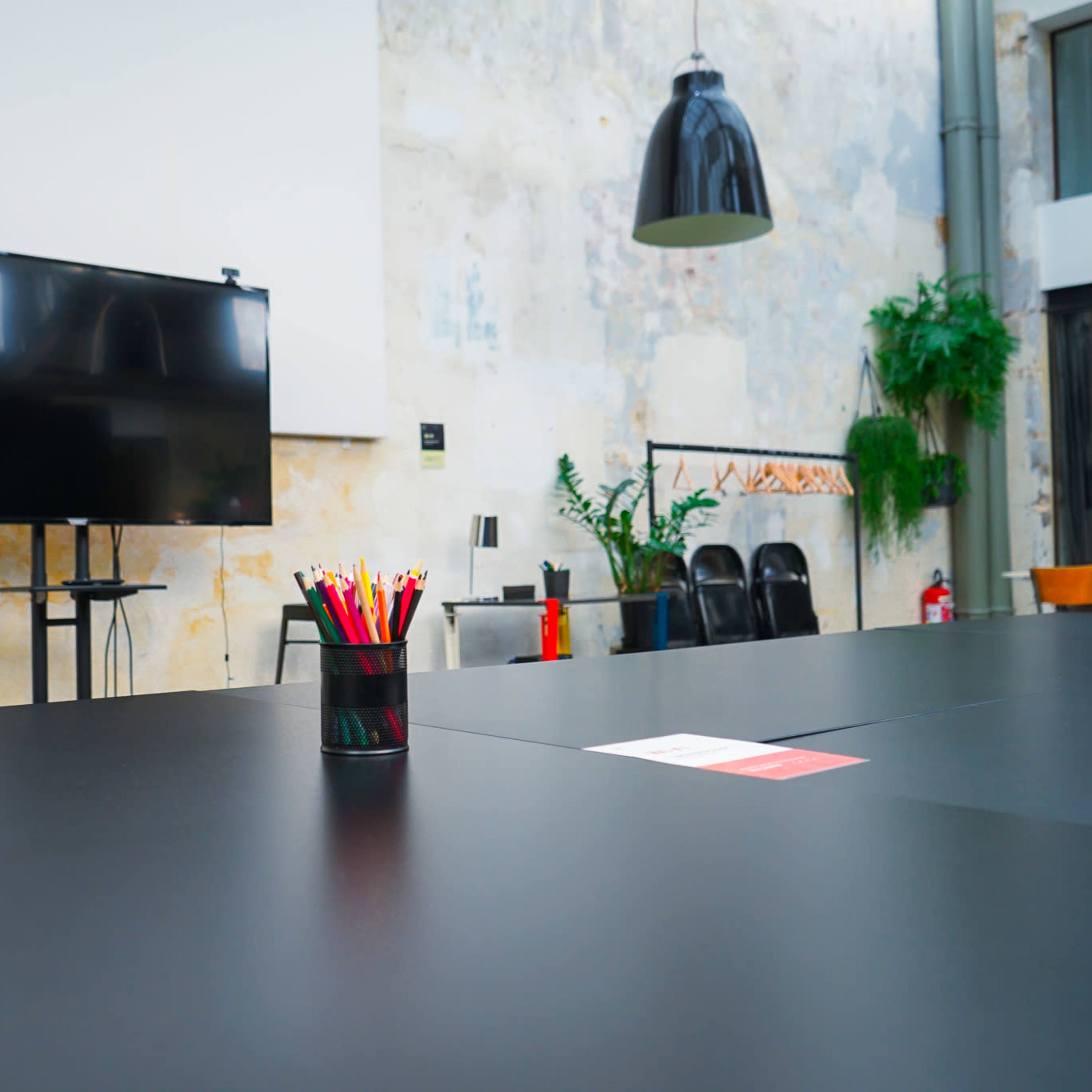 A modern conference room features a large black table, a television screen on the wall, and colorful pens arranged in a cup.