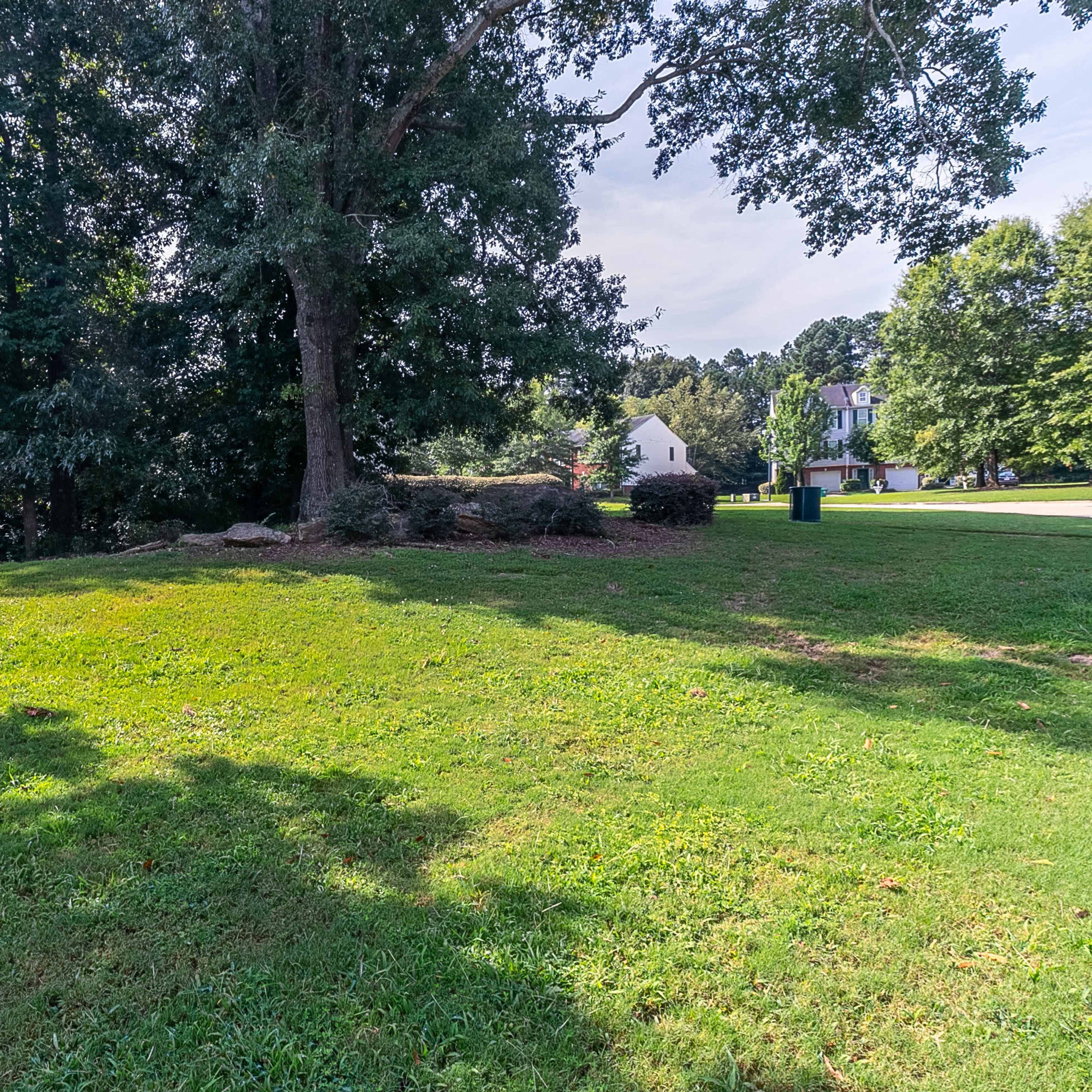 A grassy area with trees and shrubs, leading to a home in the background.