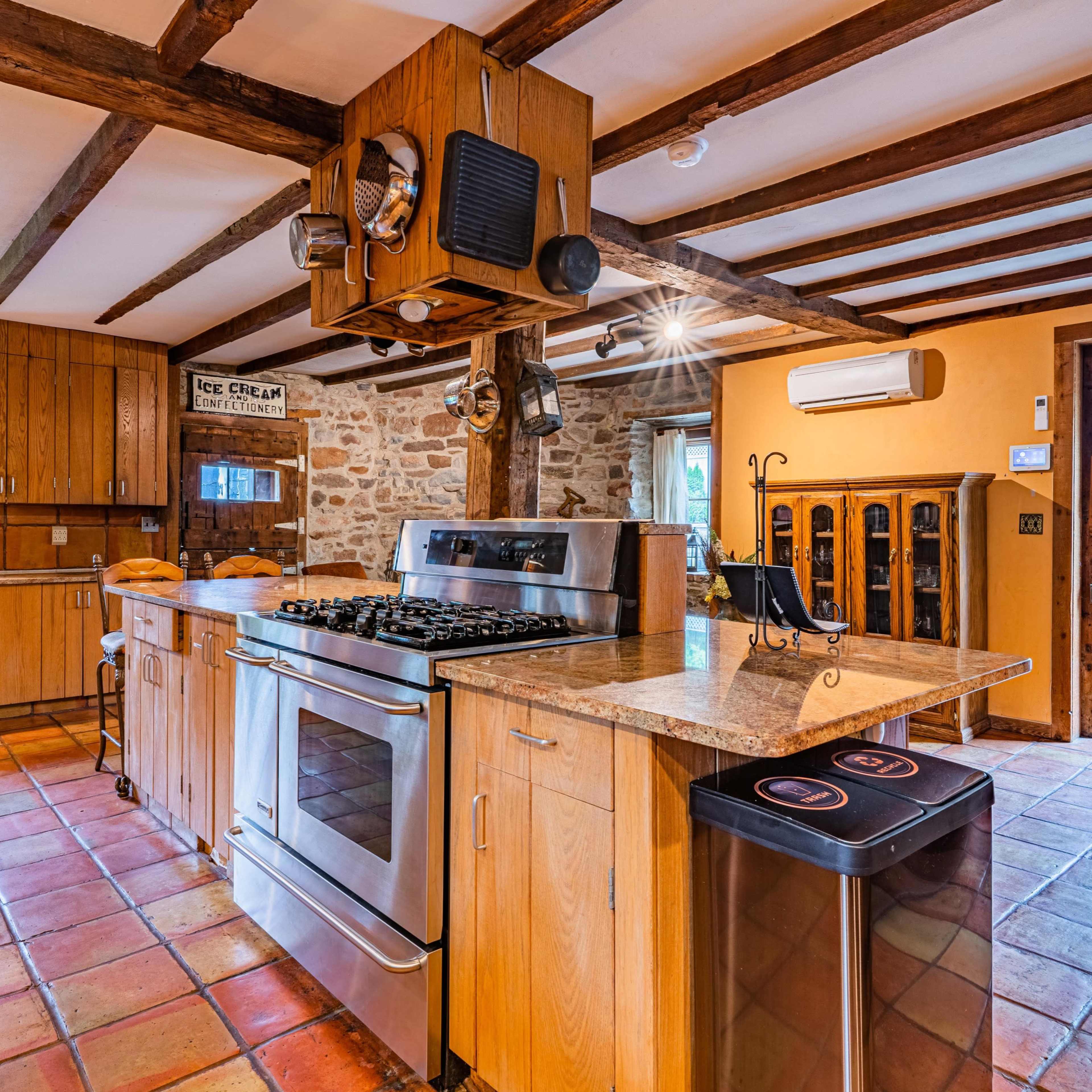 The kitchen features wooden beams, stone walls, a gas stove with an overhead hood, and tiled flooring.