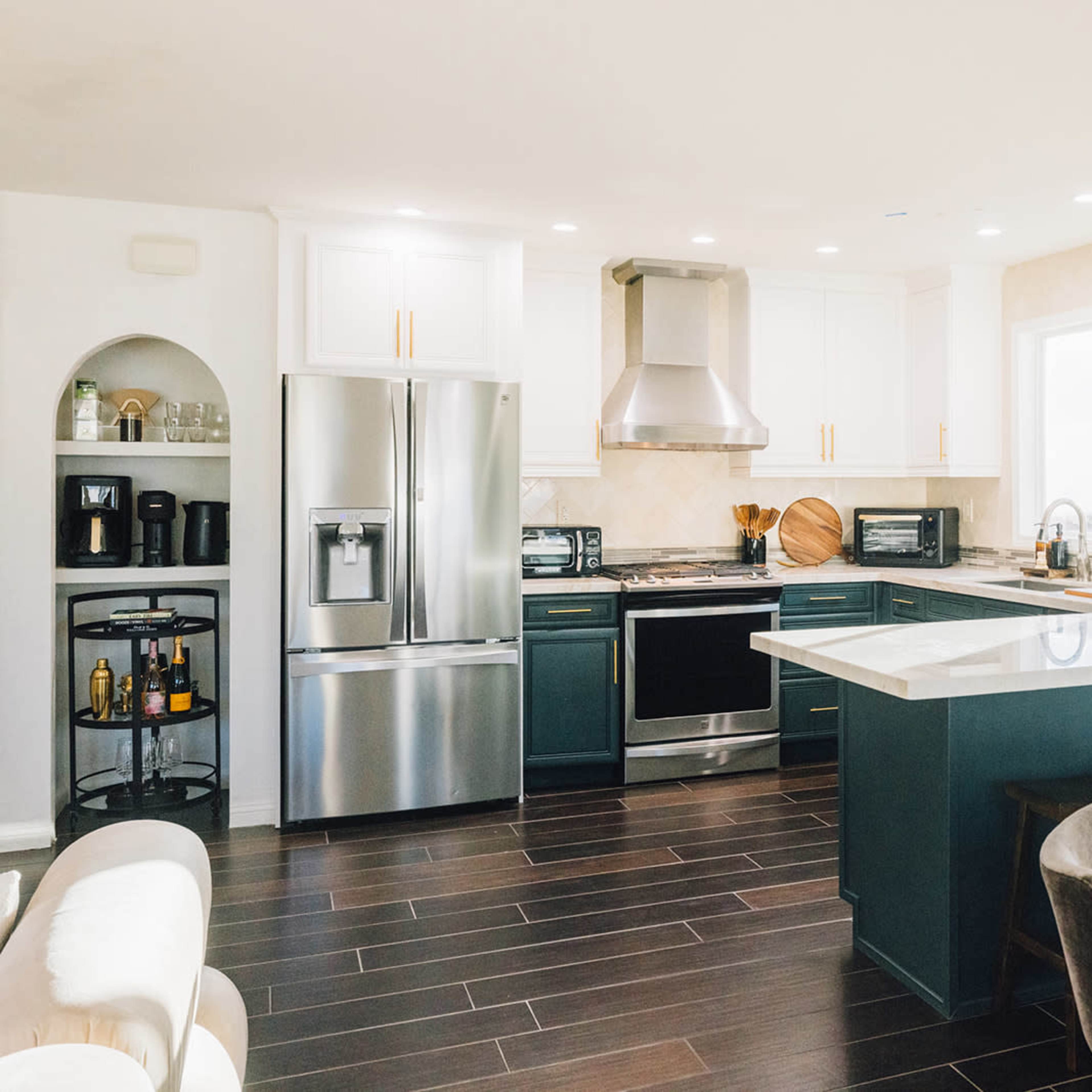 The kitchen features modern appliances, a large island with seating, and a mix of dark and light cabinetry.