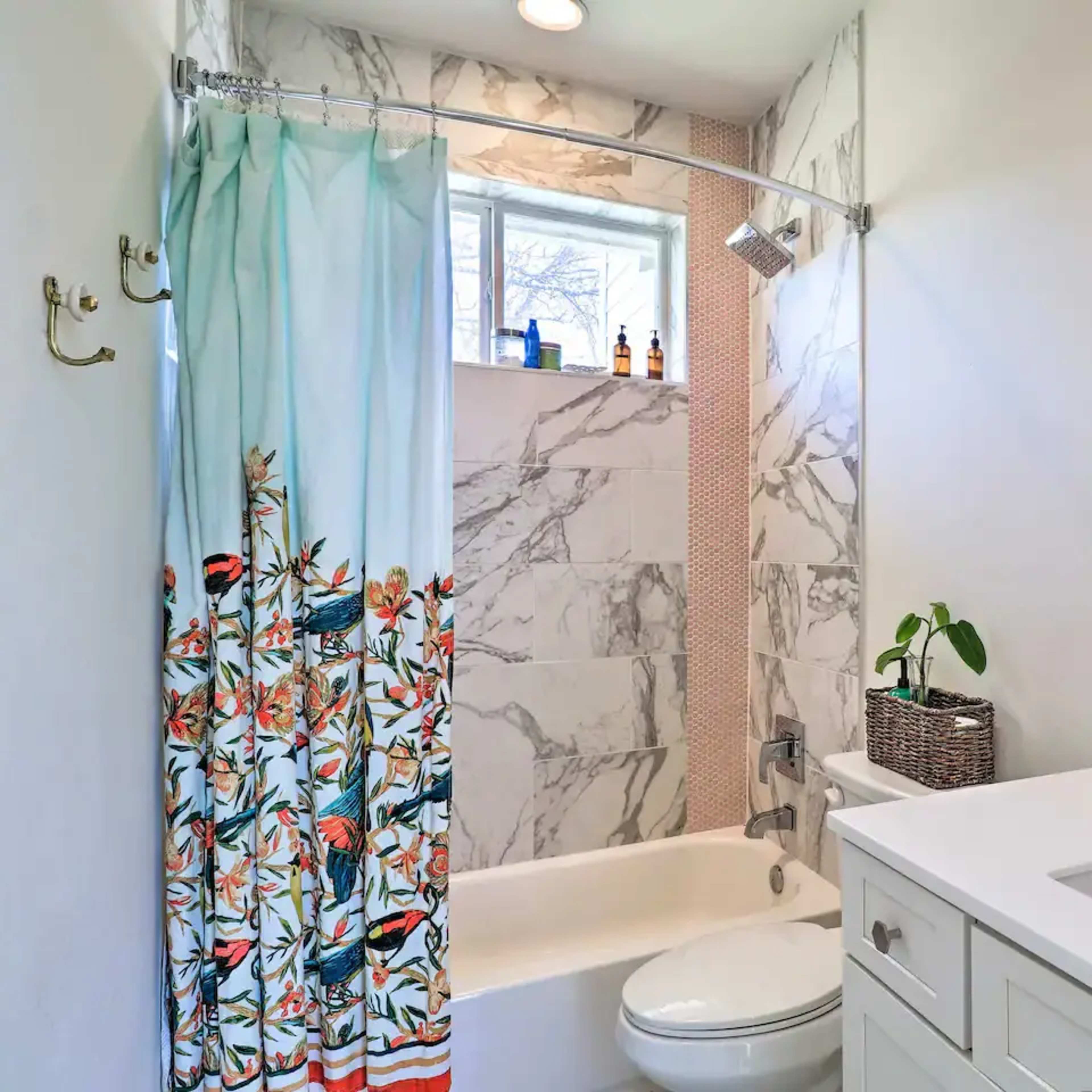 A bathroom features a bathtub with a floral shower curtain, a white countertop sink, and marble tile accents.