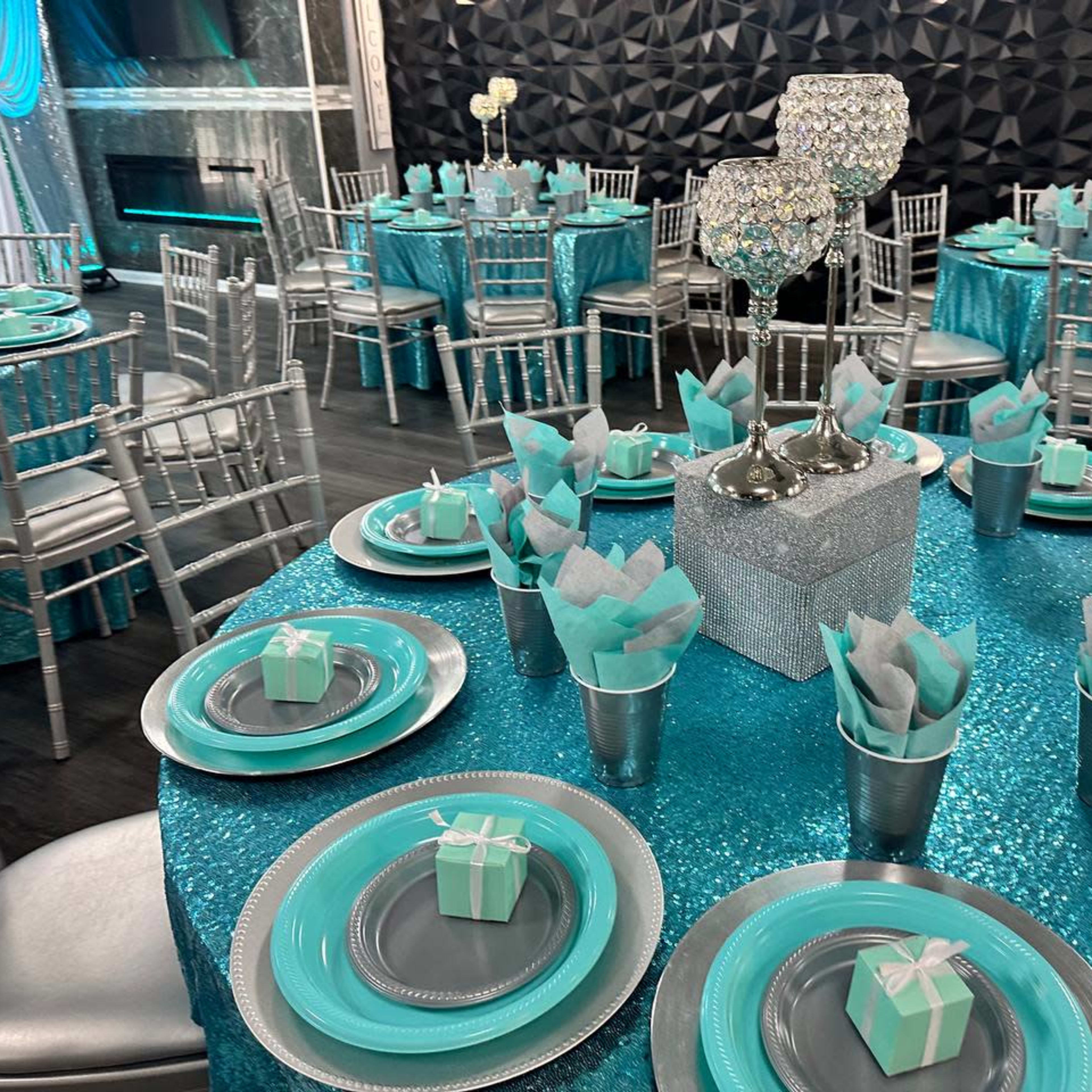 A banquet hall decorated with teal and silver table settings, featuring round tables with sparkling tablecloths and elegantly arranged dishes and centerpieces.