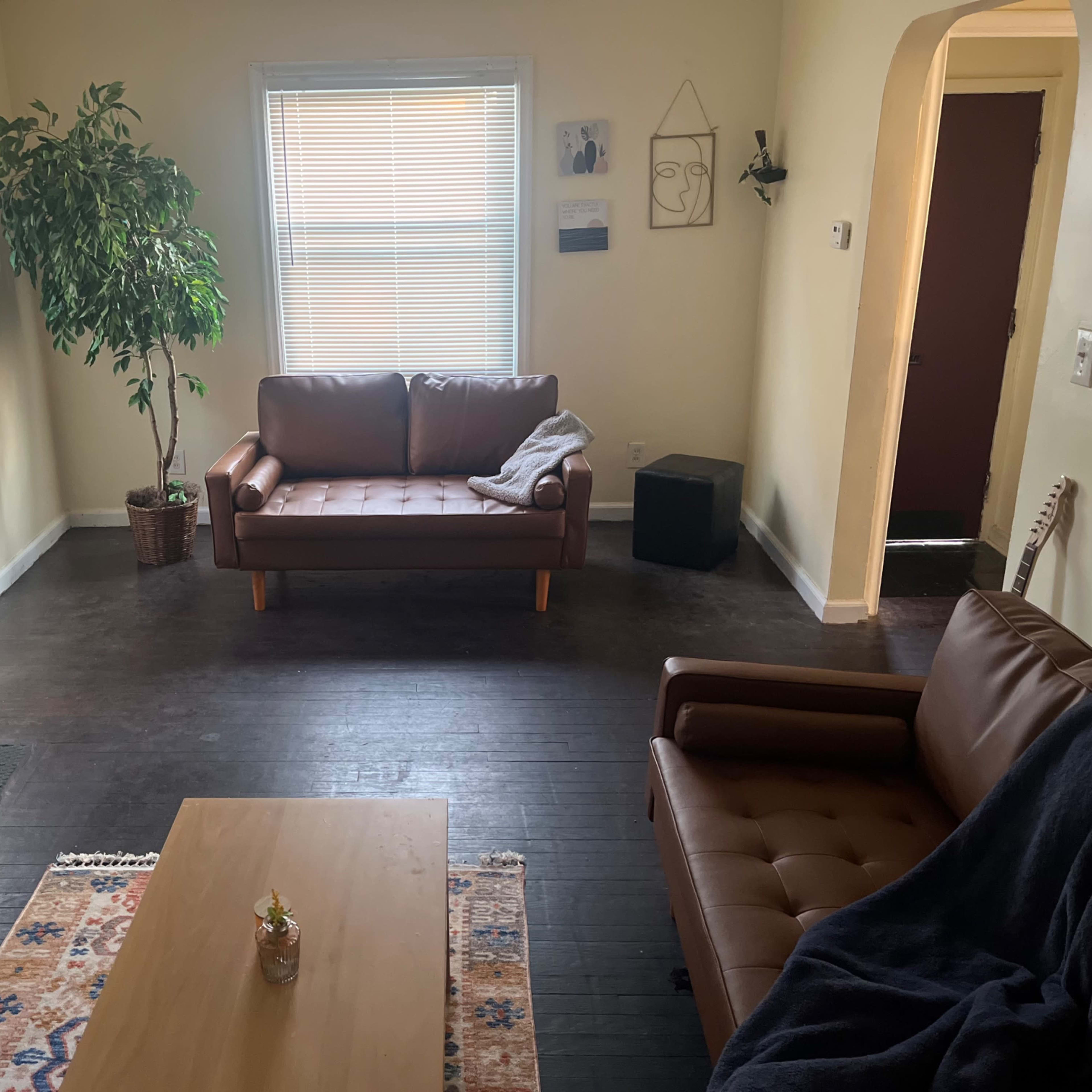 A living room with two brown sofas, a coffee table, a potted plant, and a doorway leading to another room.