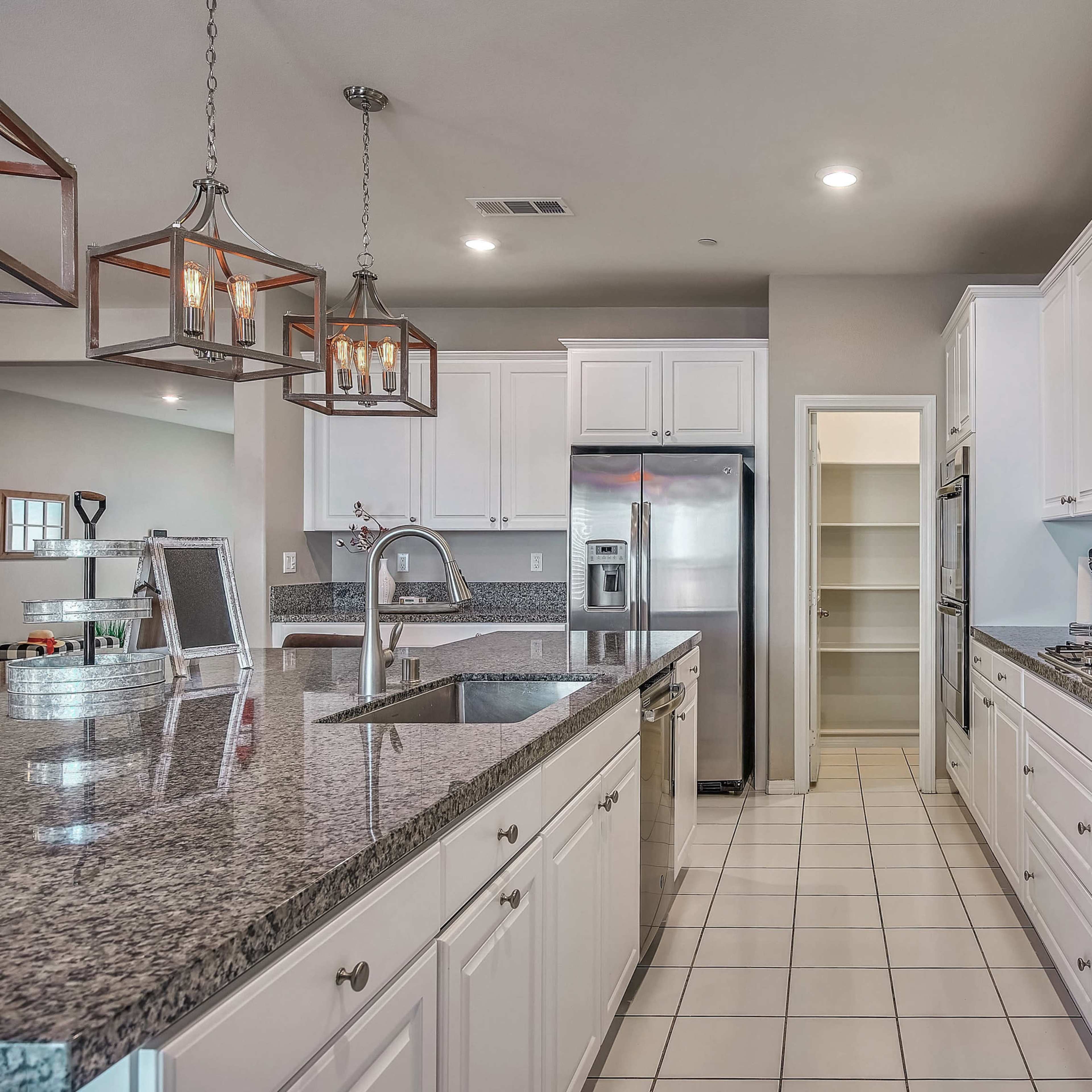 A modern kitchen features white cabinets, granite countertops, stainless steel appliances, and tile flooring.