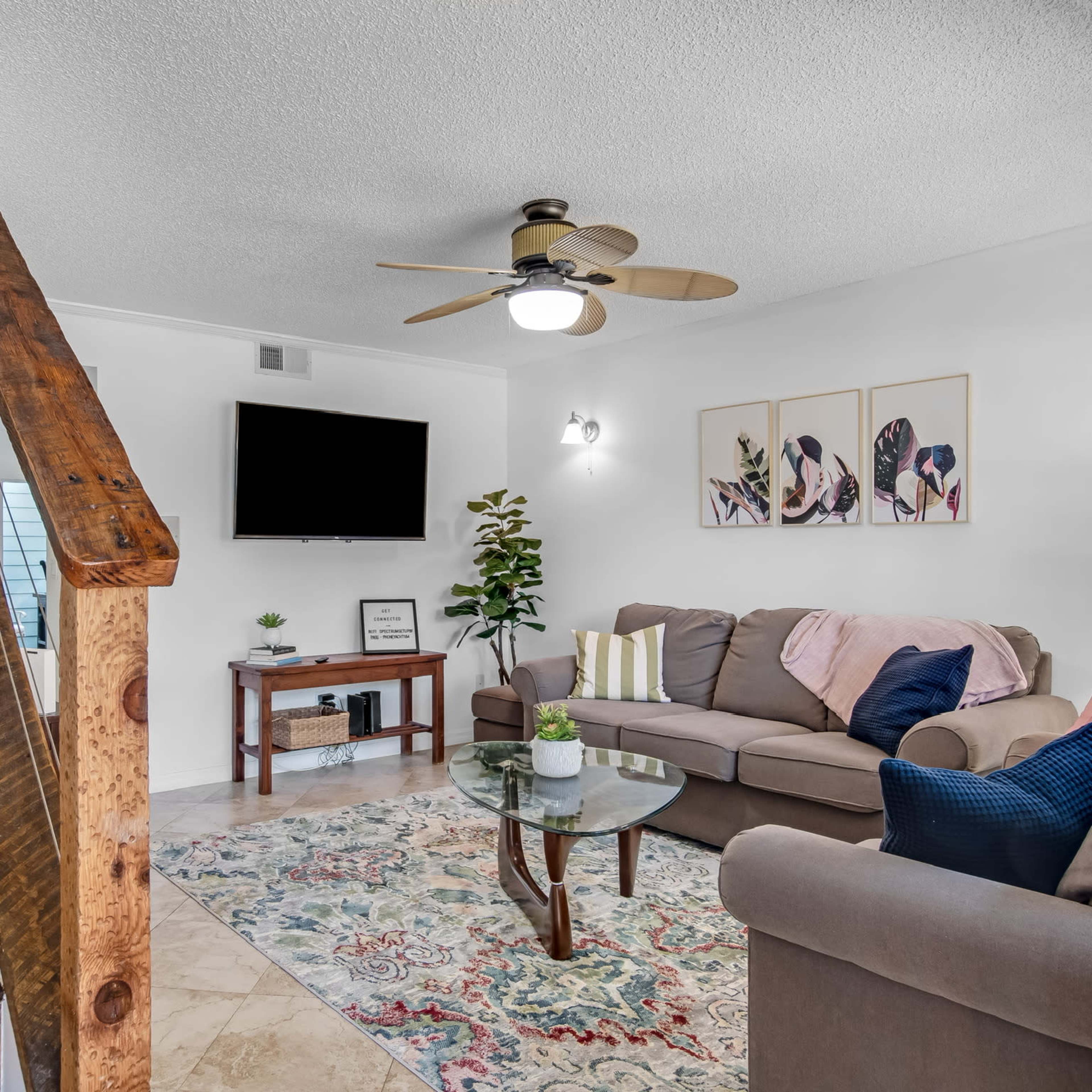A living room features a sofa, coffee table, and a staircase leading to another level, with a wall-mounted TV and decorative wall art.