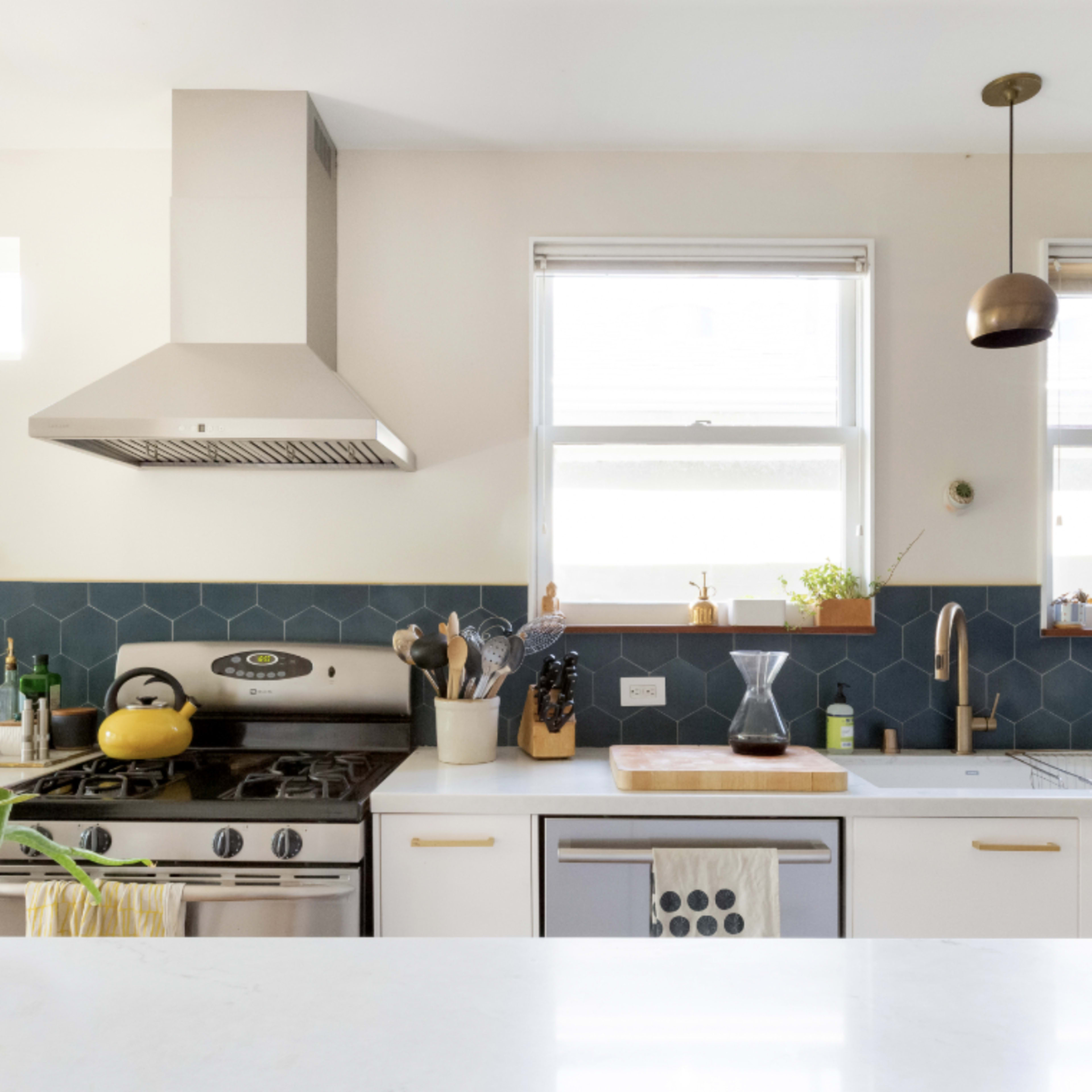 A bright kitchen features a mix of stainless steel appliances, white cabinetry, and green hexagonal tiles on the walls.