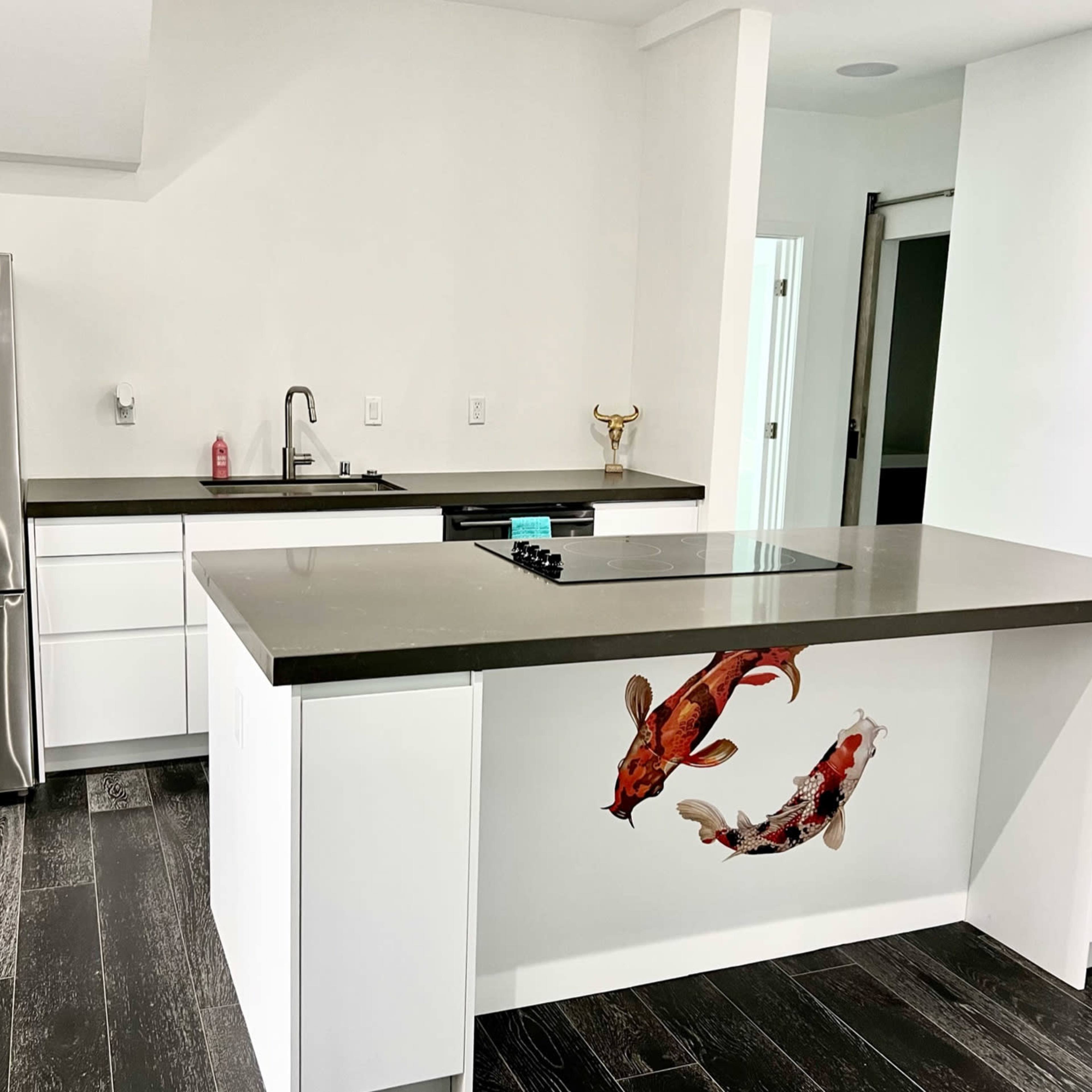 A modern kitchen with stainless steel appliances, a dark countertop, and a kitchen island featuring a decorative design of koi fish.
