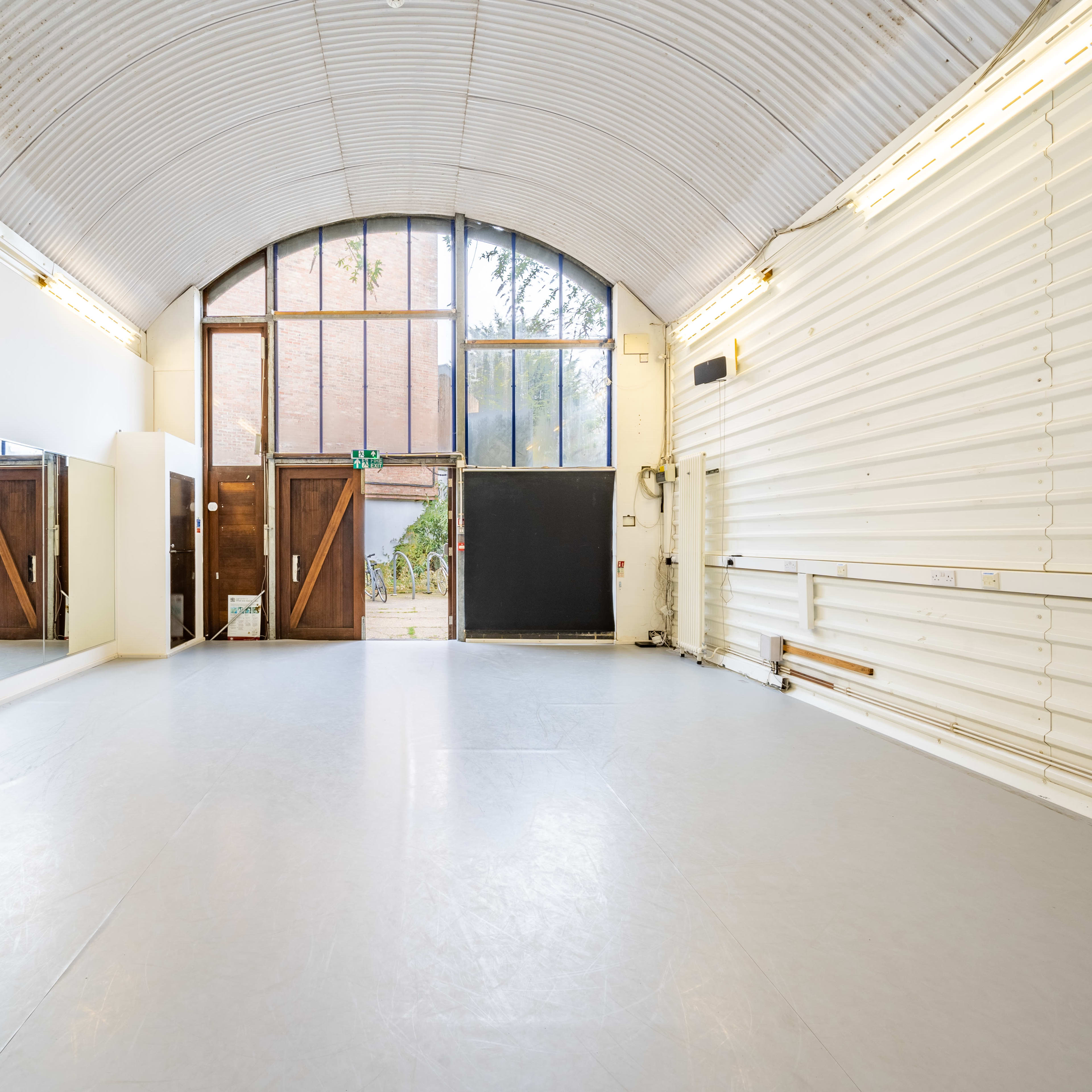A spacious dance studio with mirrored walls, large windows, and a light gray floor.
