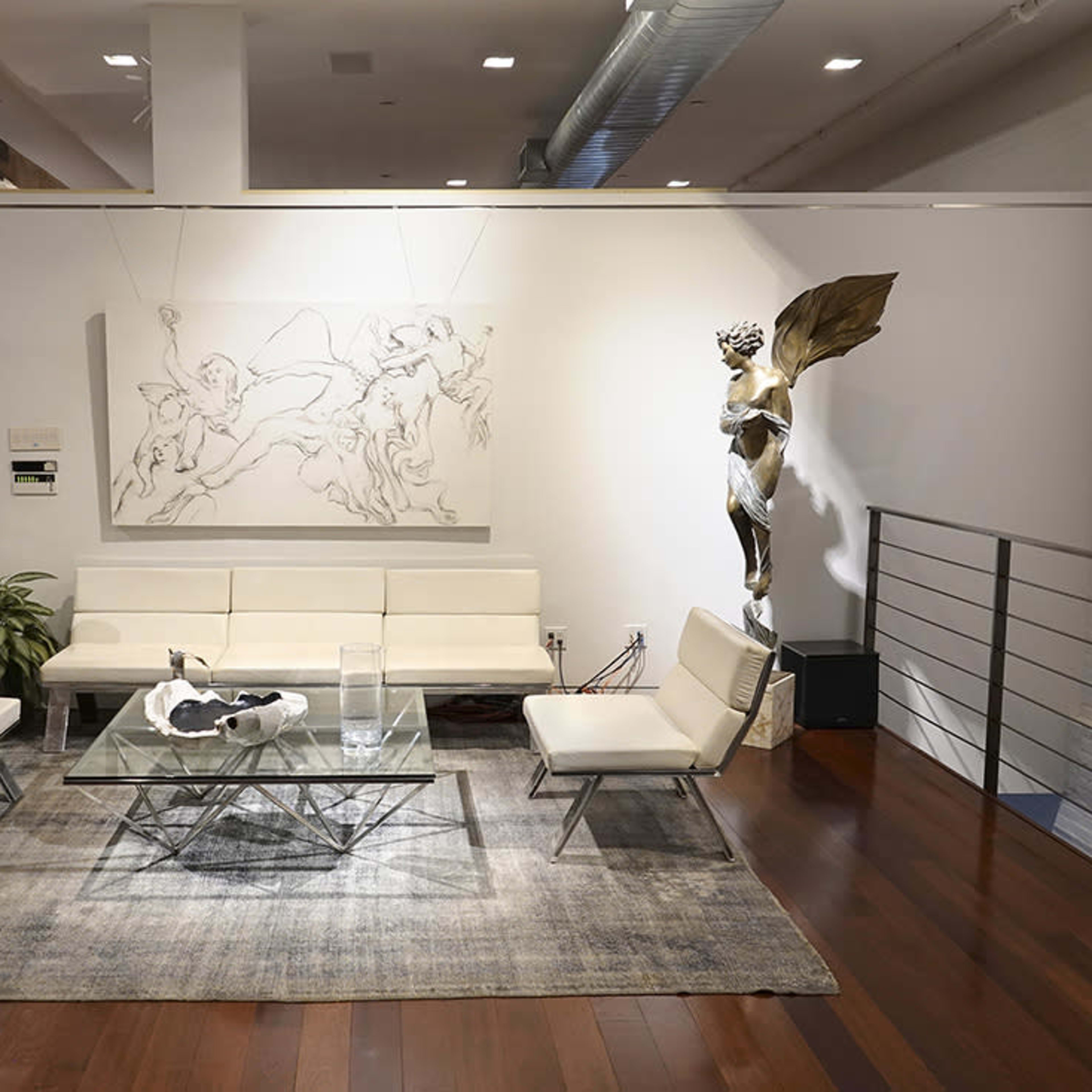 A modern interior space featuring a white couch, glass coffee table, and a sculpture, with wooden flooring and a large wall art piece.