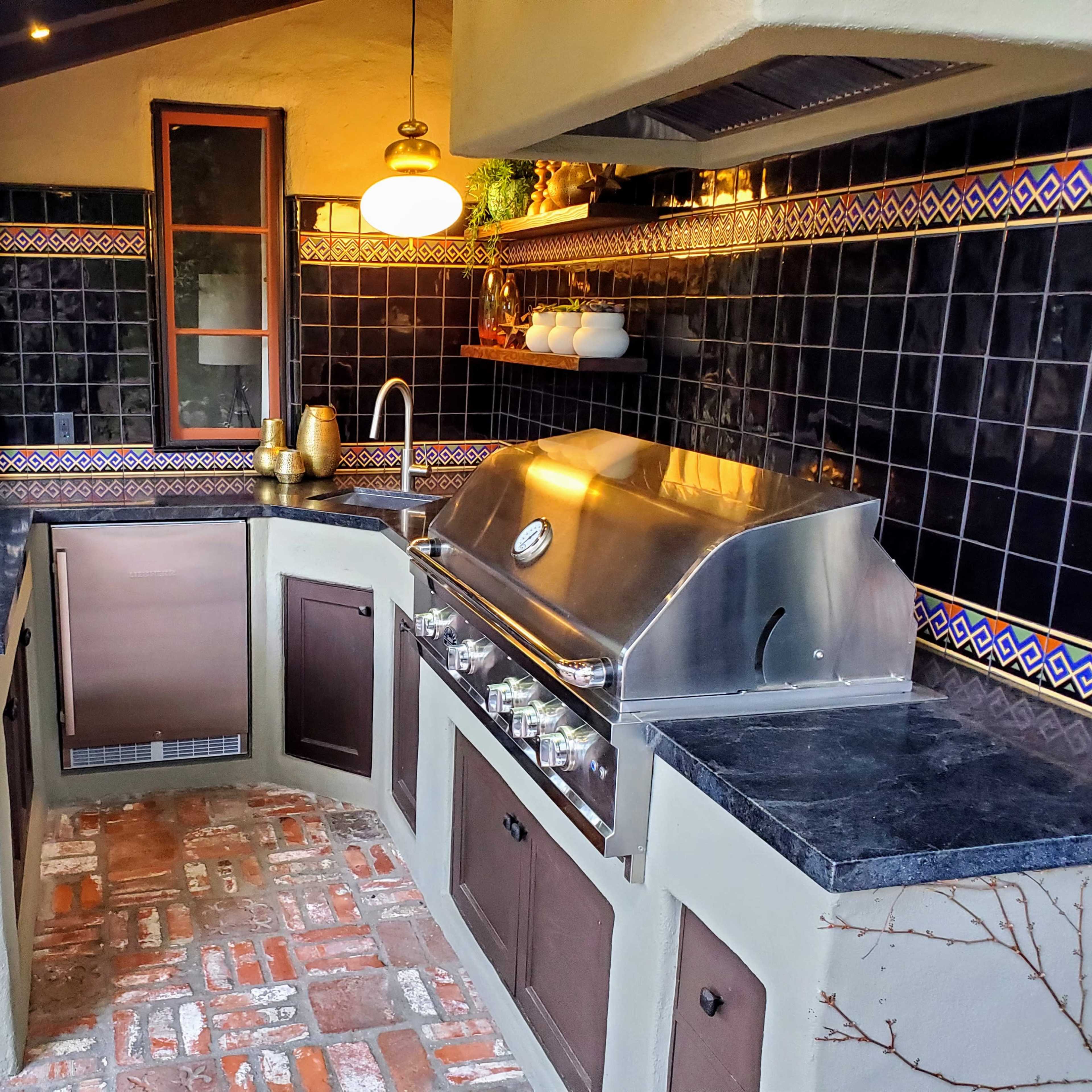 An outdoor kitchen featuring a stainless steel grill, dark countertops, and decorative tile accents.