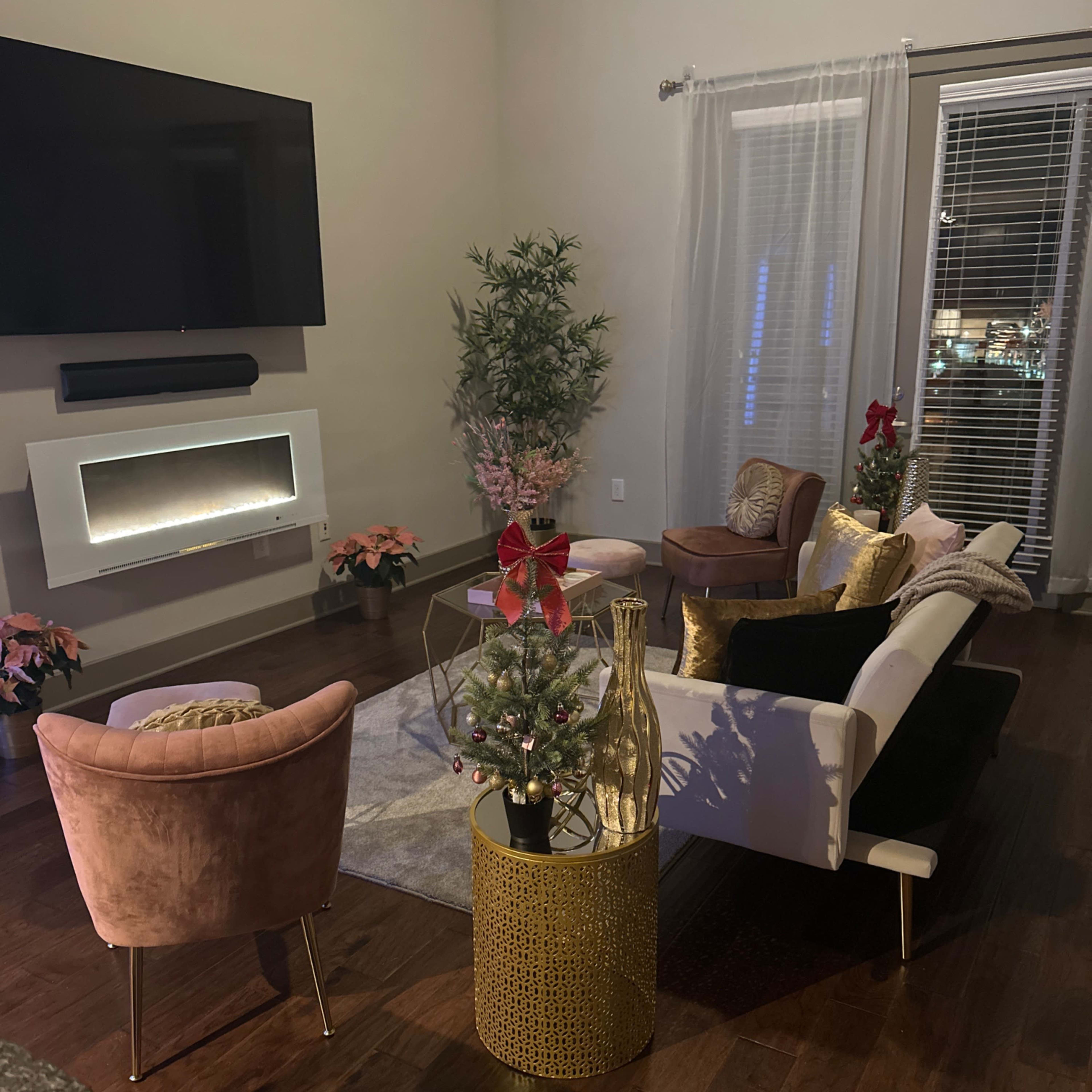 The living room features a modern seating area with a decorative electric fireplace, a circular rug, and two small Christmas trees adorned with bows.