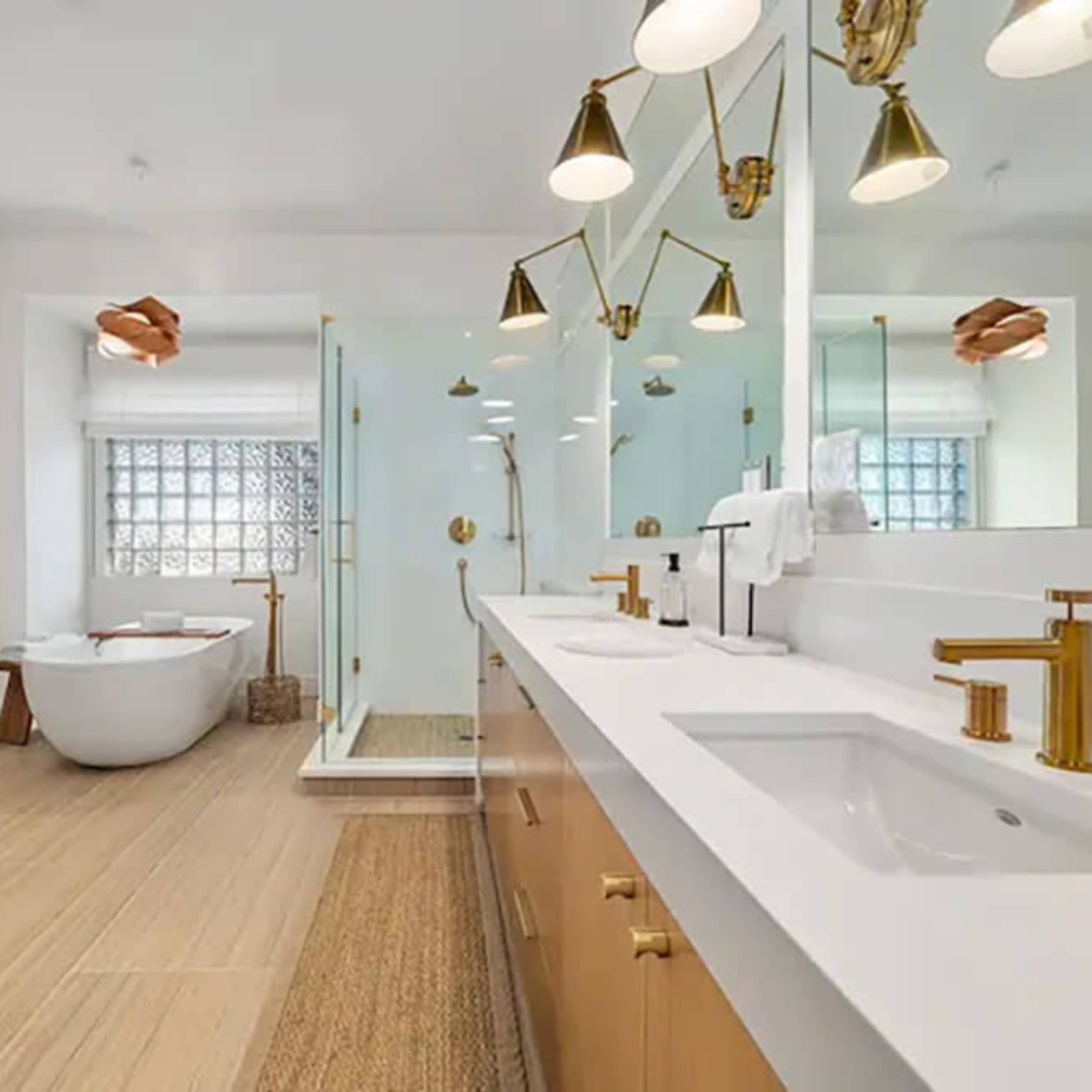A modern bathroom featuring a double sink vanity with gold fixtures, a freestanding bathtub, and a glass shower enclosure.