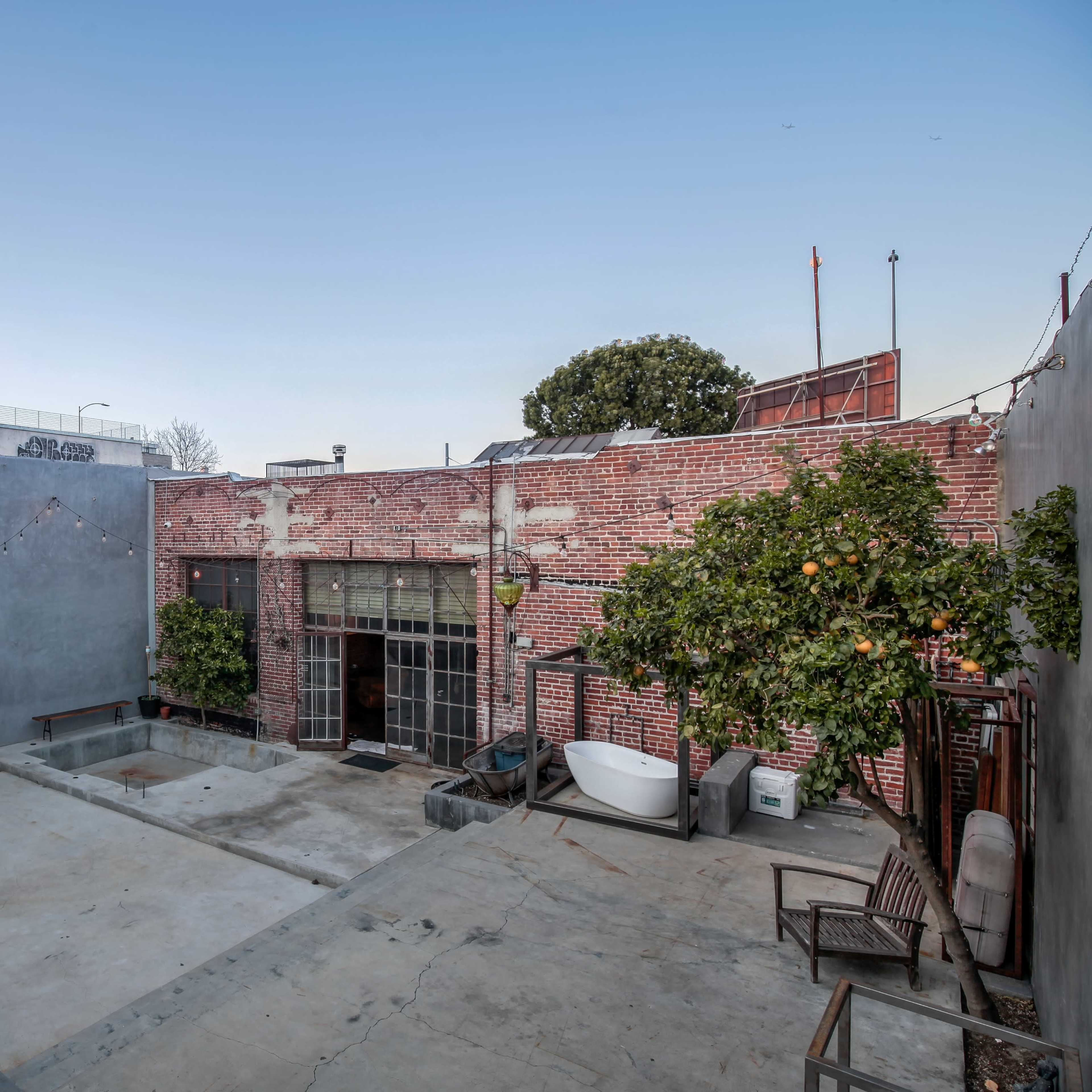 A spacious outdoor area with a concrete surface, brick walls, a tree with oranges, and a warehouse-style glass door.