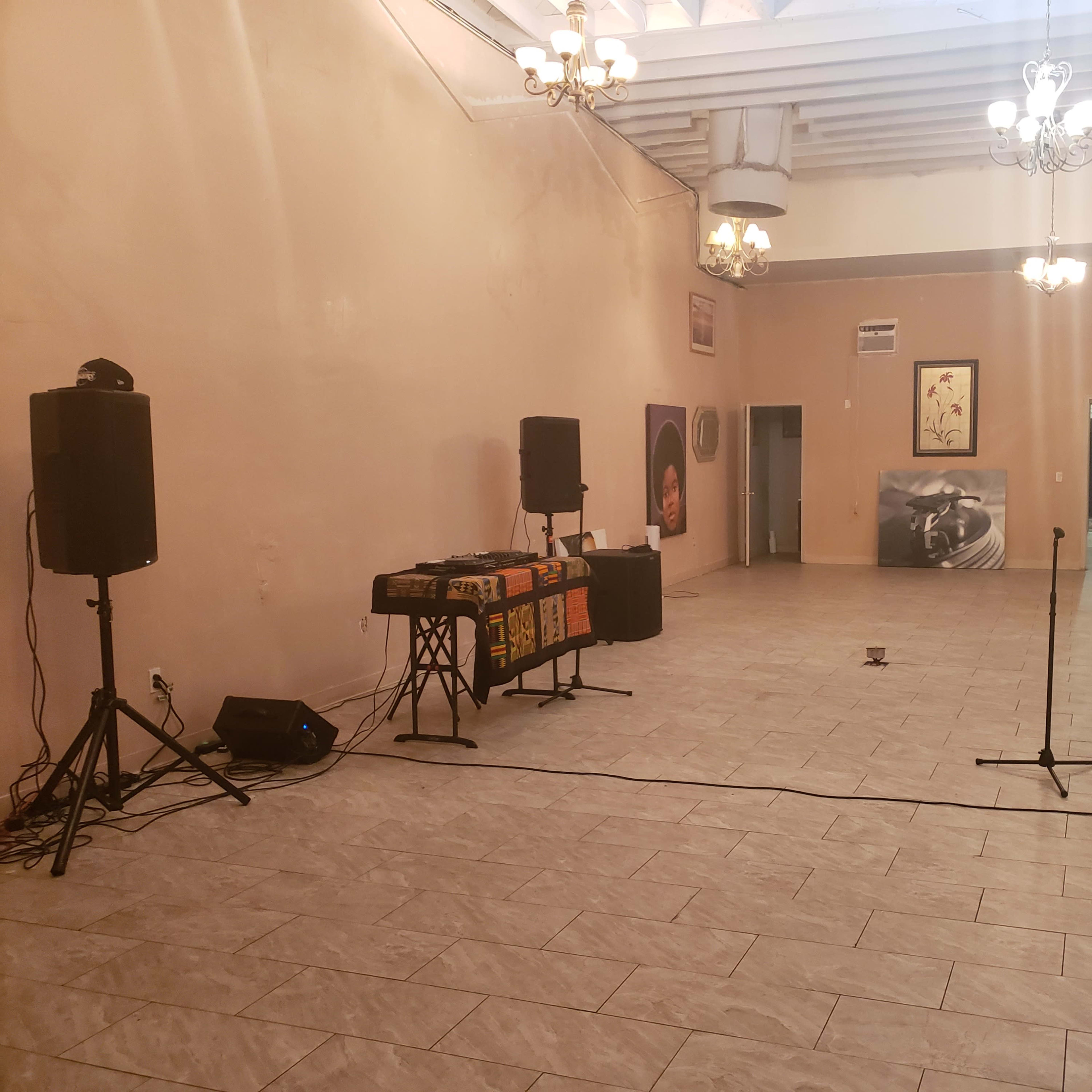 An empty room with two large speakers, a DJ table, a microphone stand, and mirrors on one wall.
