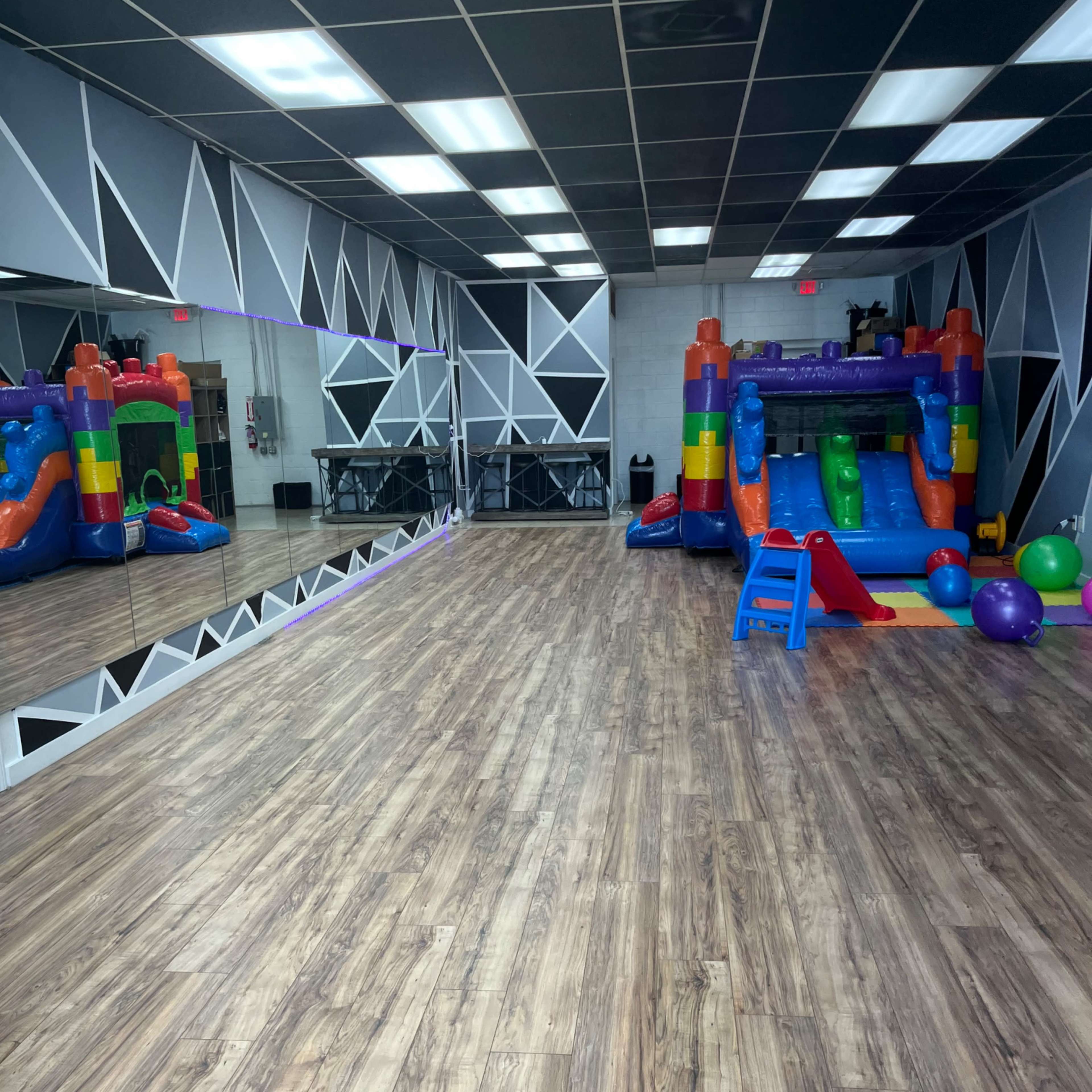 An indoor play area featuring a colorful inflatable bounce house on one side and a large mirror along the wall, with wooden flooring throughout.