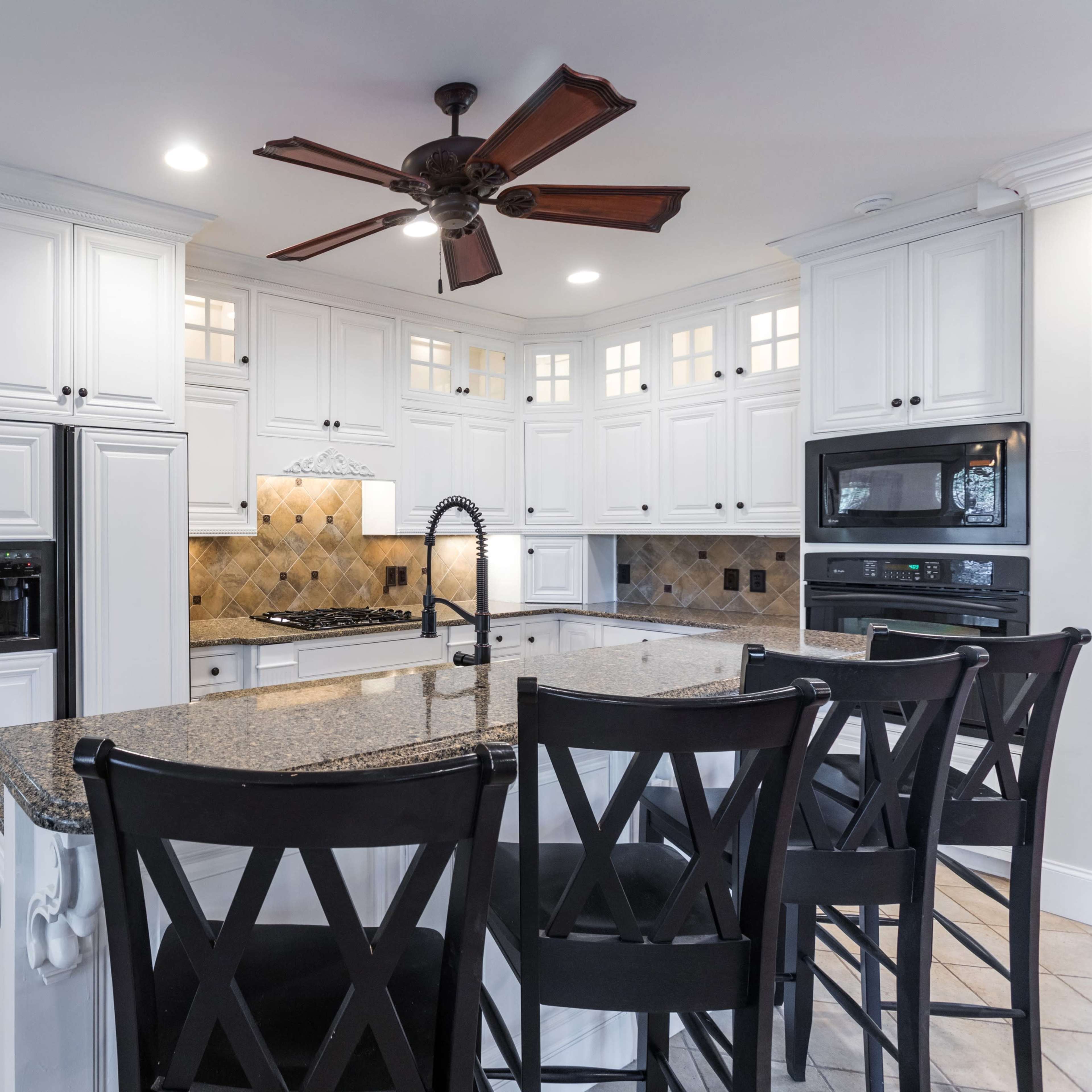 A spacious kitchen features white cabinetry, a large island with black bar stools, and a tile backsplash.